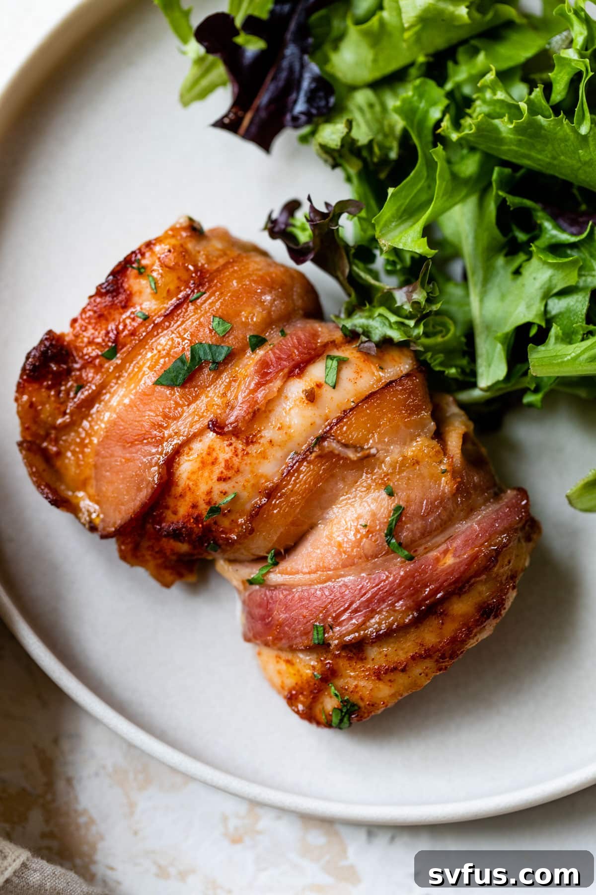 bacon-wrapped chicken thigh on a plate with fresh lettuce leaves, ready to be served