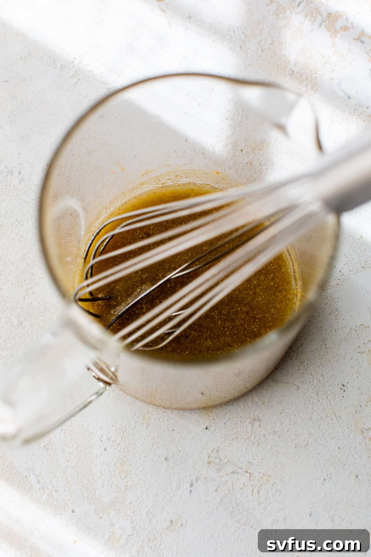 A small glass bowl containing olive oil, freshly squeezed lime juice, salt, and cumin, being whisked together to form the salsa dressing.