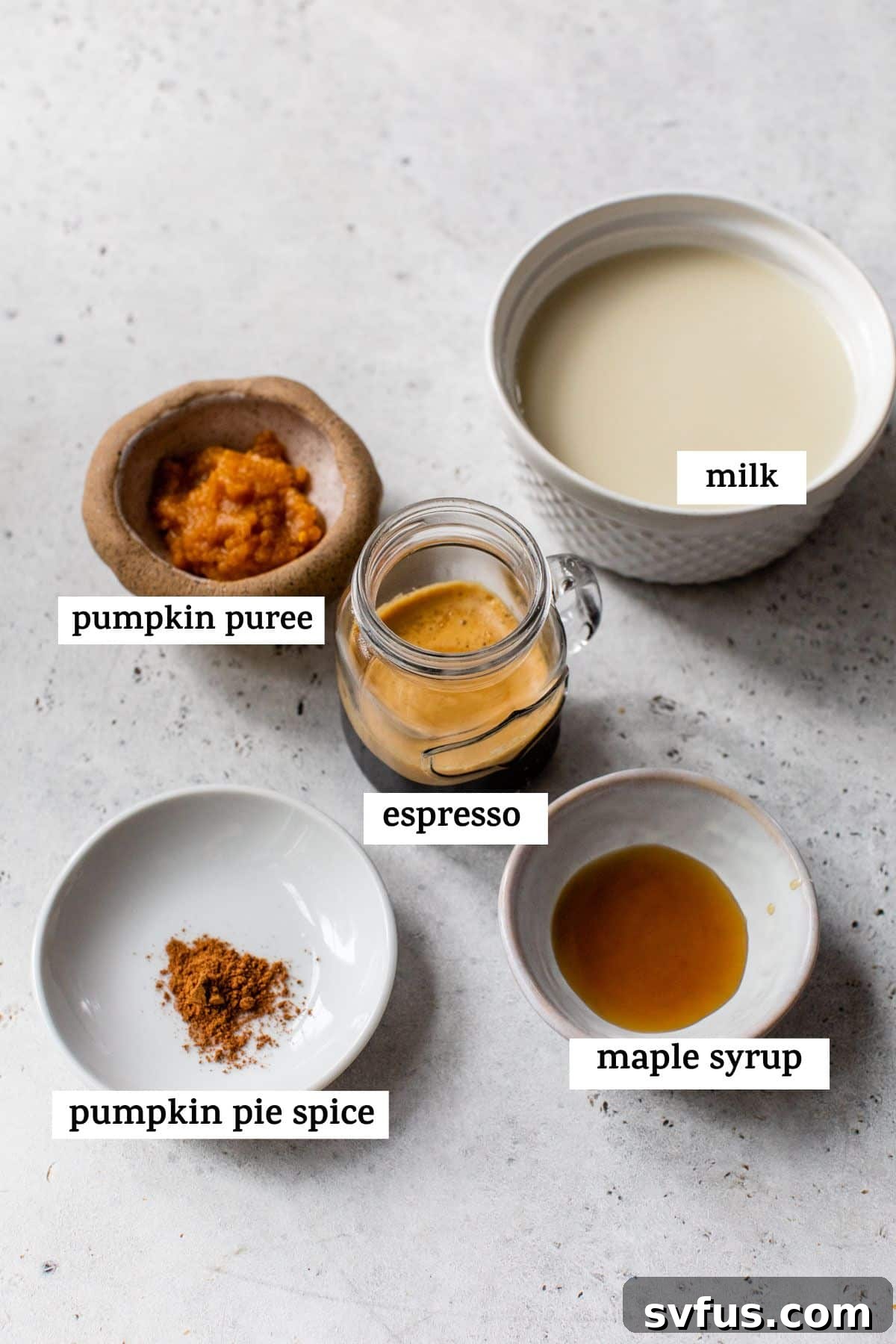 A simple array of five core ingredients laid out on a table: pumpkin puree, milk, espresso, pumpkin pie spice, and maple syrup, ready for making a delicious latte.