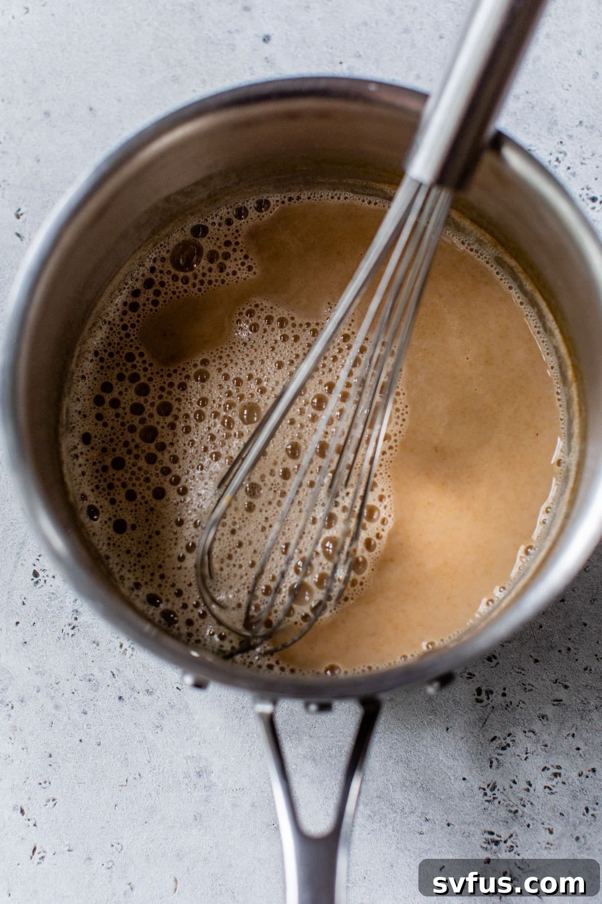All the milk ingredients for the pumpkin spice latte, including pumpkin puree, milk, maple syrup, and pumpkin pie spice, are in a saucepan and being whisked together.