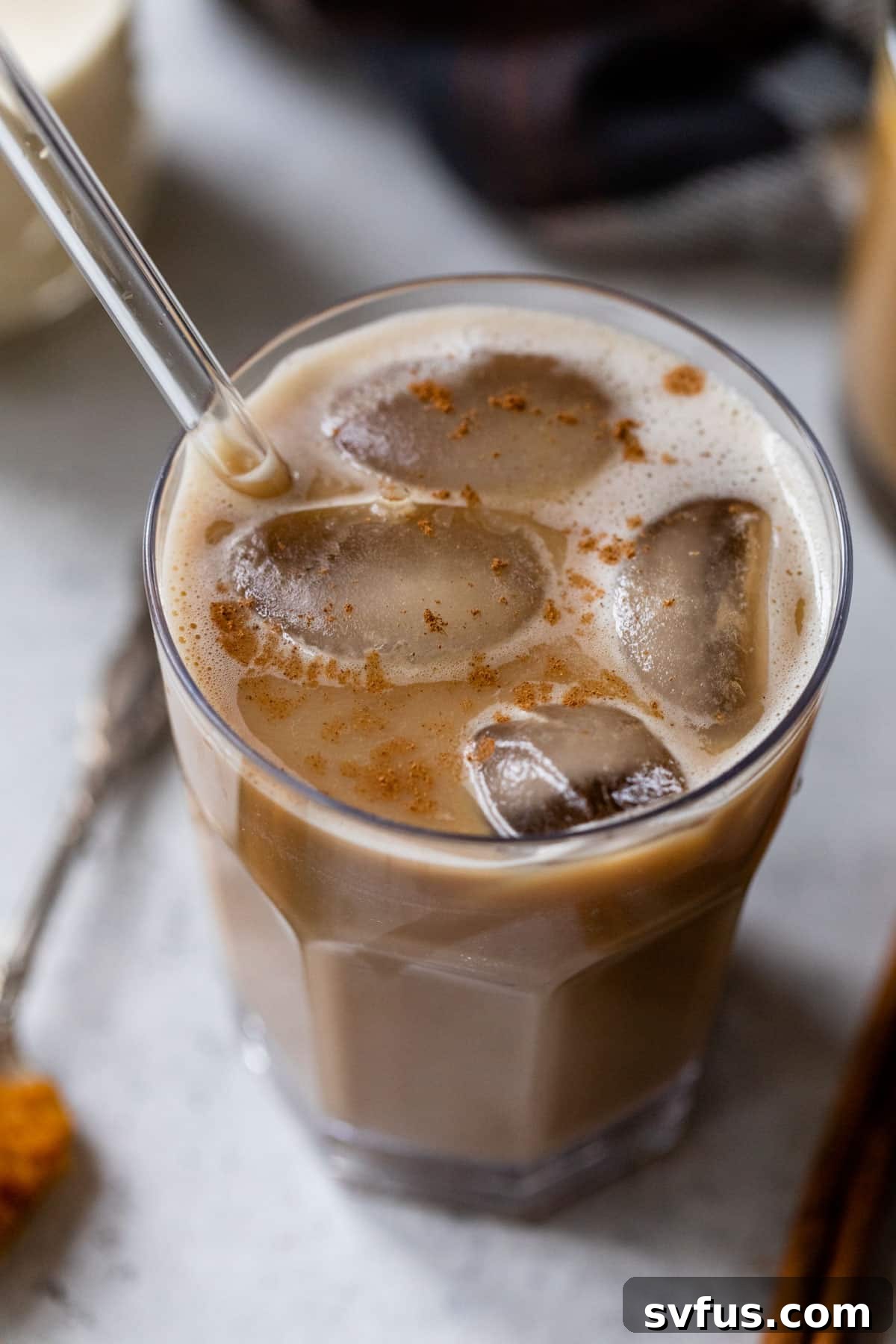 A side view of an iced pumpkin spice latte served in a glass with a straw, capturing the layered appearance.
