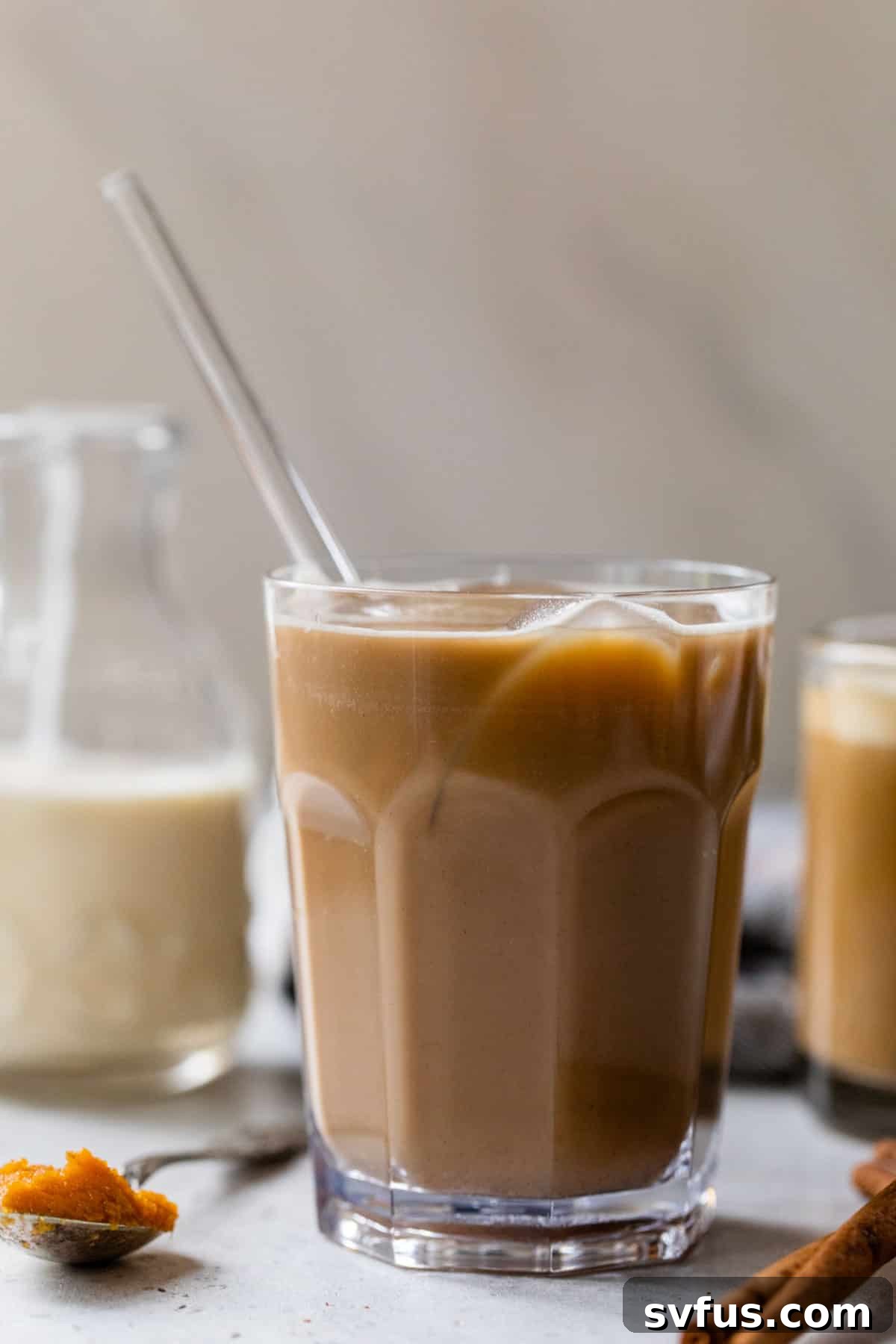 A delicious iced pumpkin spice latte, seen from a side angle, served in a tall glass with a straw, showcasing its beautiful layers and refreshing appeal.