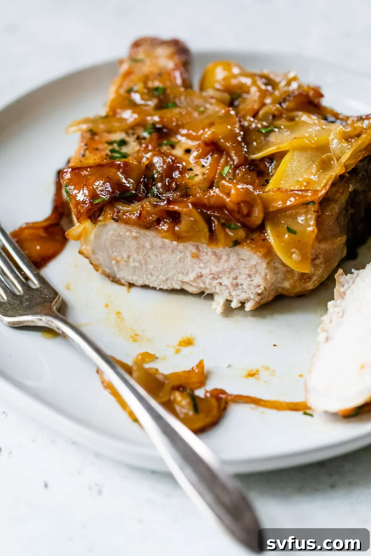apple pork chops on a plate with a fork and with a portion of the pork chop cut off