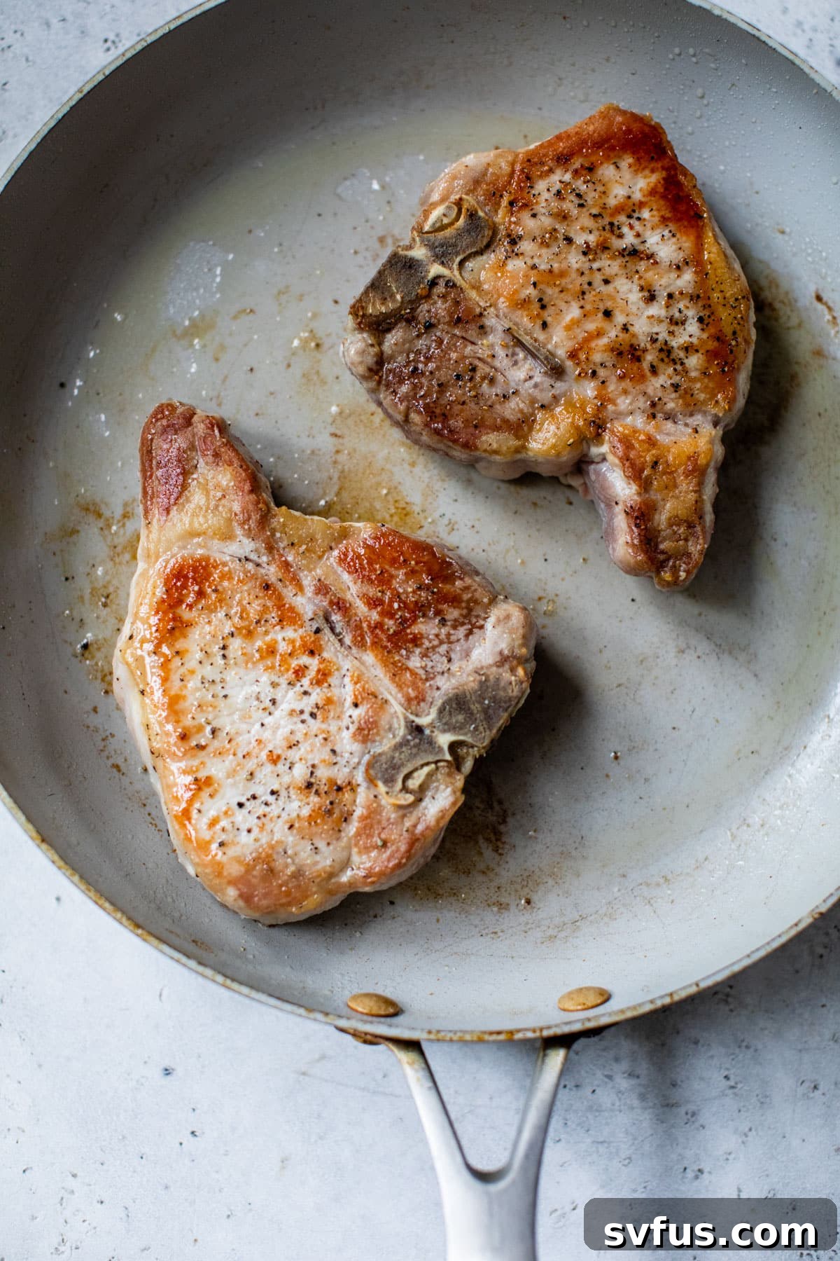 two pork chops cooking in a skillet