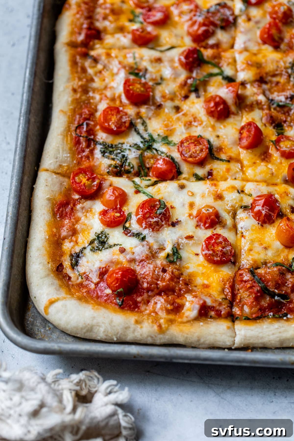 Close-up of a freshly baked sheet pan pizza, showing a golden crust and melted cheese.