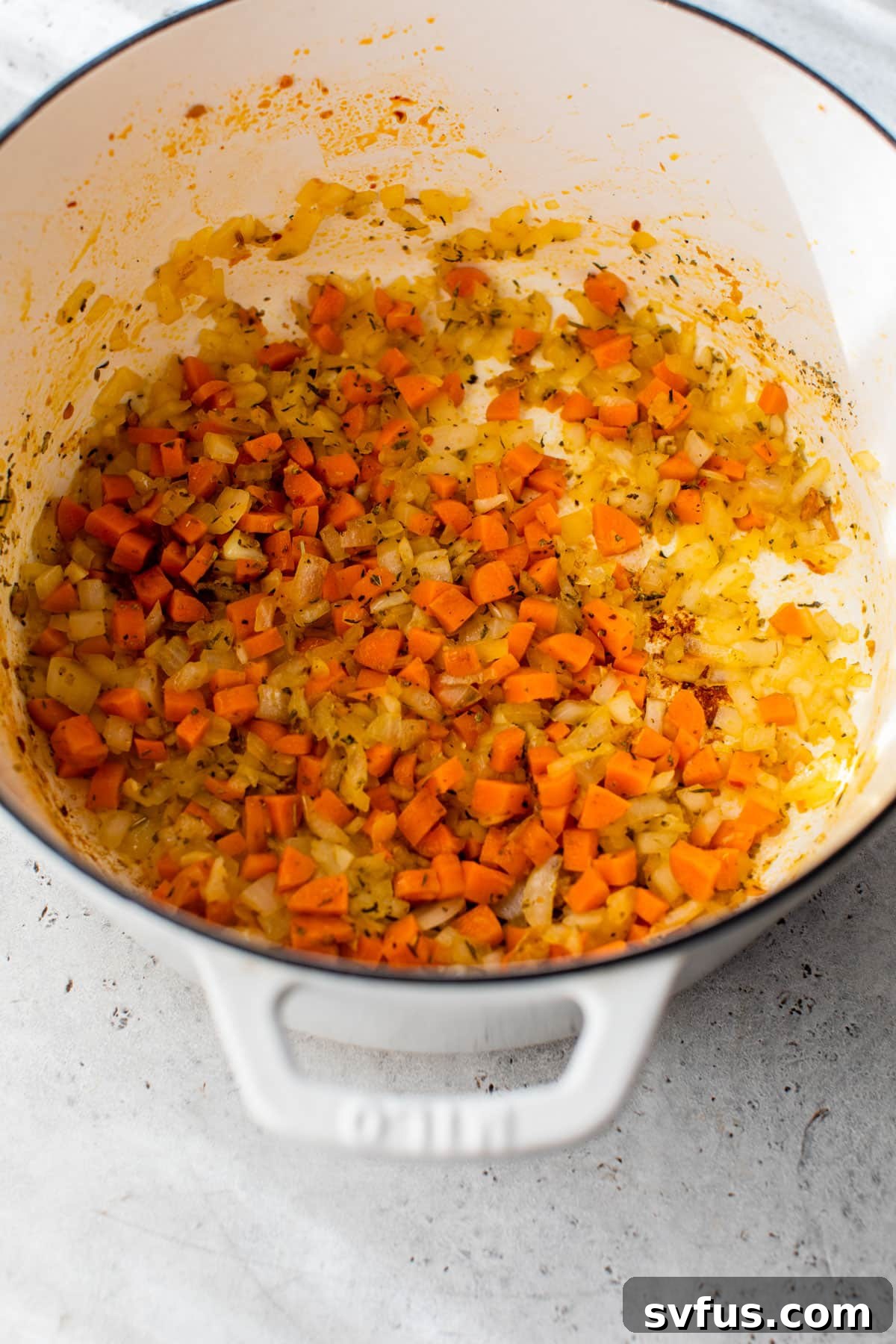 Diced onions and carrots sautéing in a Dutch oven with spices.