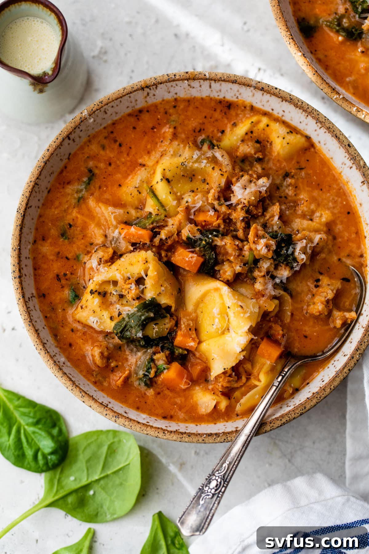 A close-up shot of creamy sausage tortellini soup in a bowl with a spoon.
