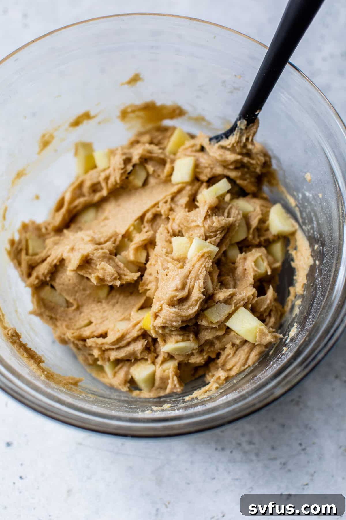 Apple blondie batter in a clear glass mixing bowl, perfectly combined and ready for baking, with a rubber spatula resting inside.