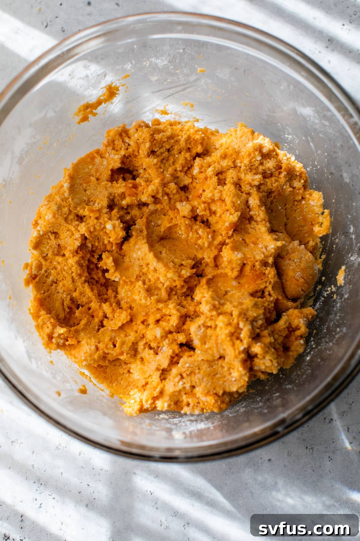 A smooth, orange-colored sweet potato gnocchi dough resting in a clear glass bowl, ready for shaping.