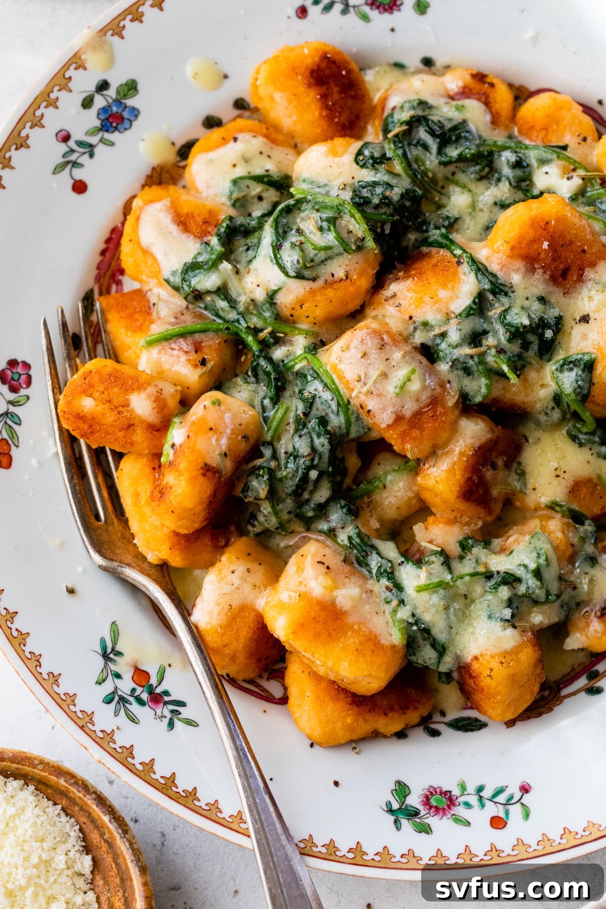 A generous serving of sweet potato gnocchi in a bowl, elegantly topped with melted butter and freshly wilted spinach, ready to be enjoyed.