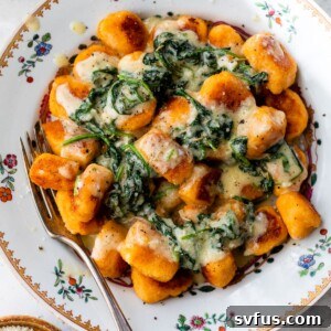 A bowl of gnocchi topped with a butter spinach sauce with a fork