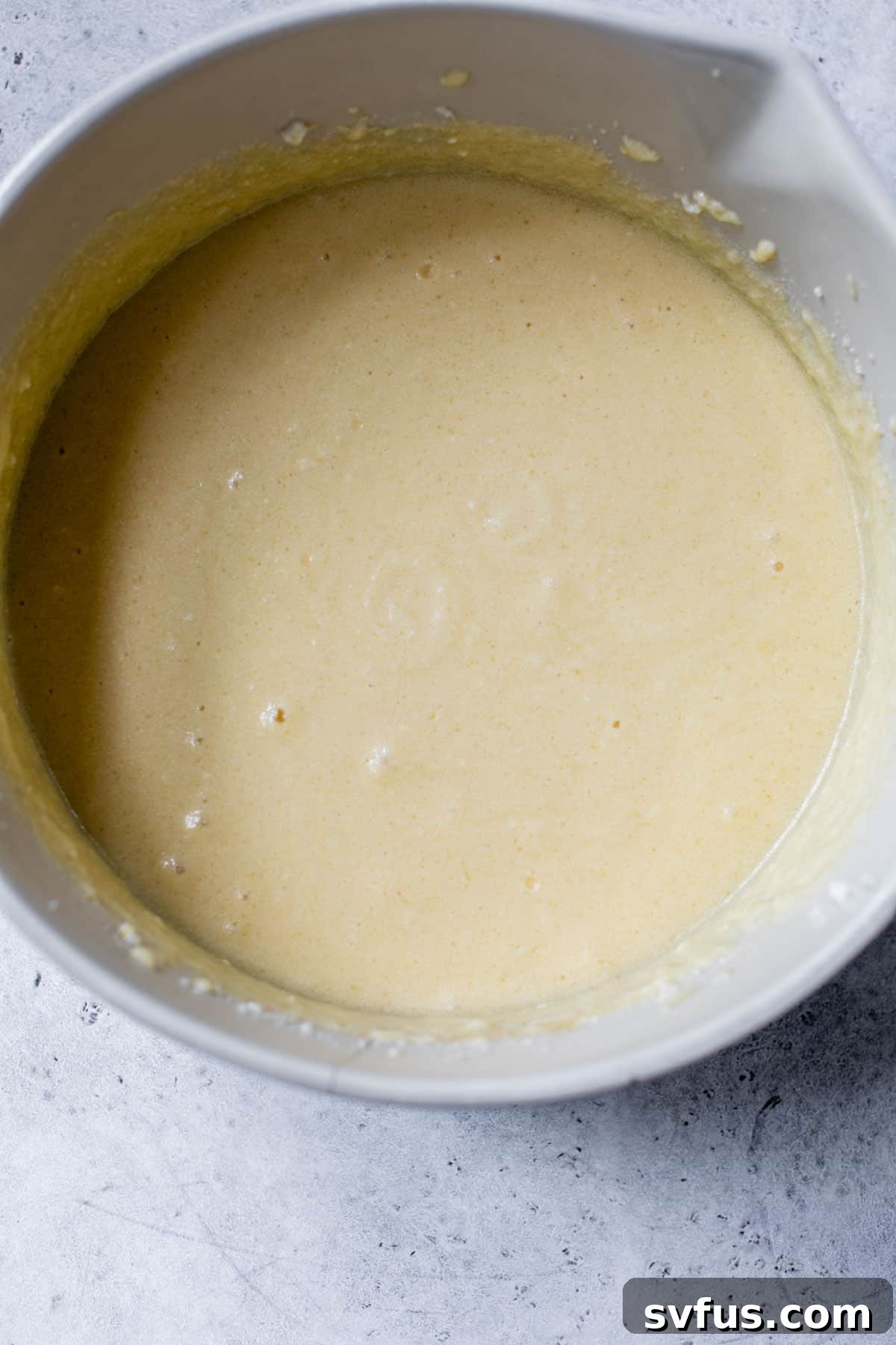Close-up shot of creamy cake batter being mixed in a large bowl, showcasing its smooth texture.