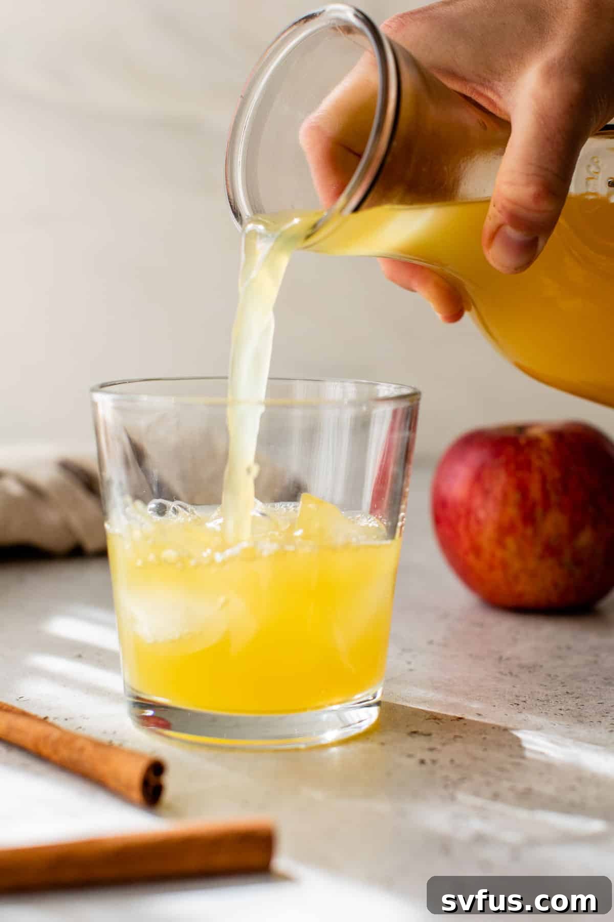 A close-up of apple cider punch being poured into a glass over ice, ready to be enjoyed.