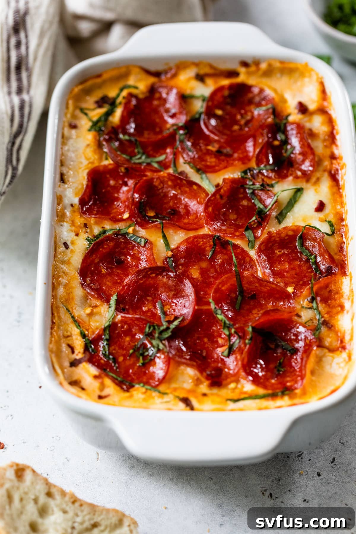 Freshly baked pizza dip in a baking dish, garnished with vibrant chopped fresh basil on top.