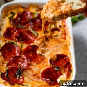 pizza dip in a baking dish with a slice of bread dipped into the dip and with chopped fresh basil on top