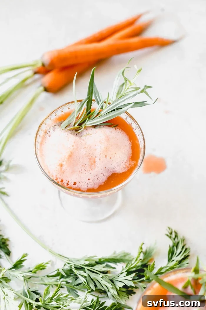 A refreshing Ginger Carrot Juice Cocktail garnished with fresh tarragon, ready to be enjoyed.