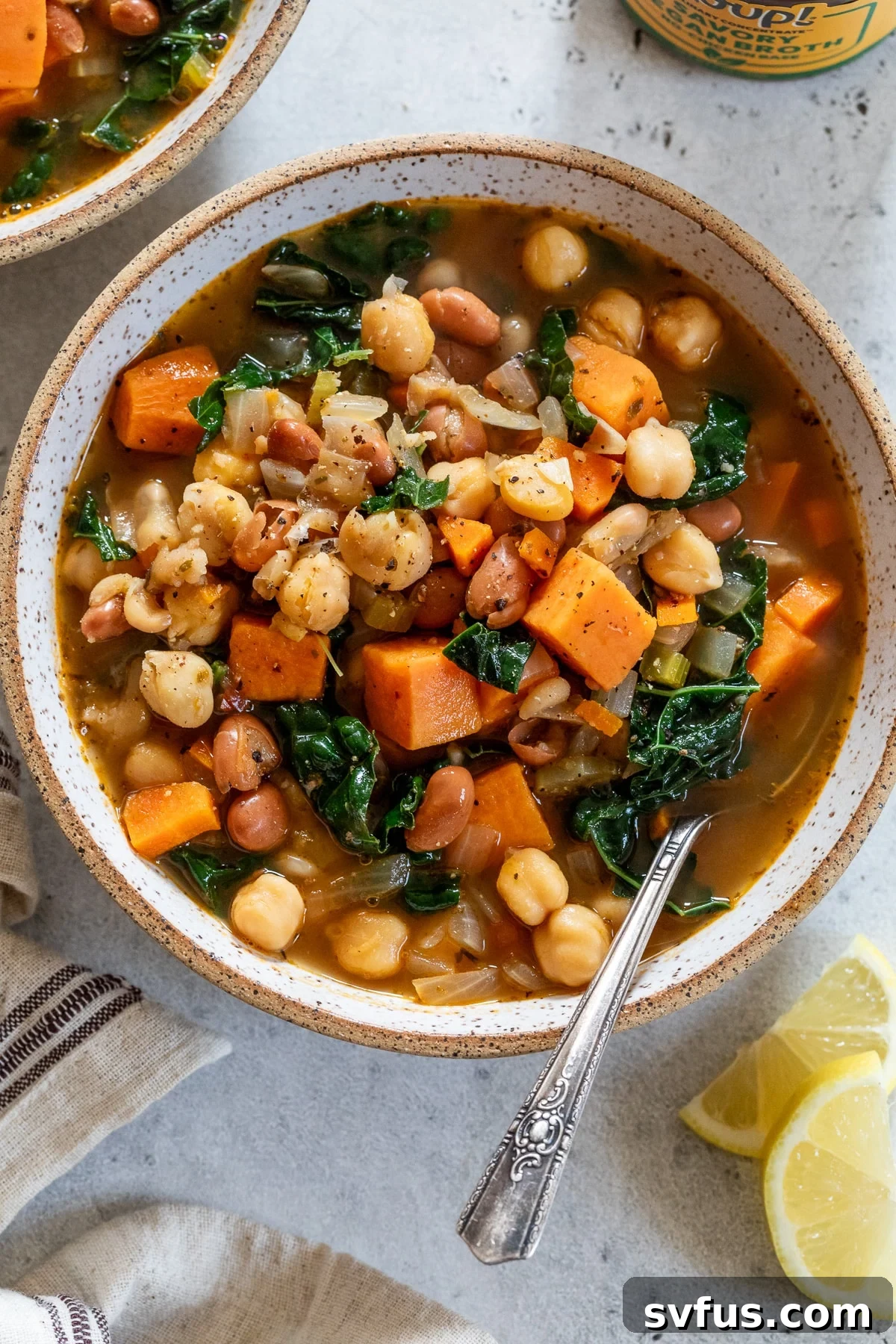 A vibrant bowl of vegan three bean soup, brimming with vegetables, beans, and sweet potatoes, garnished with a lemon wedge.