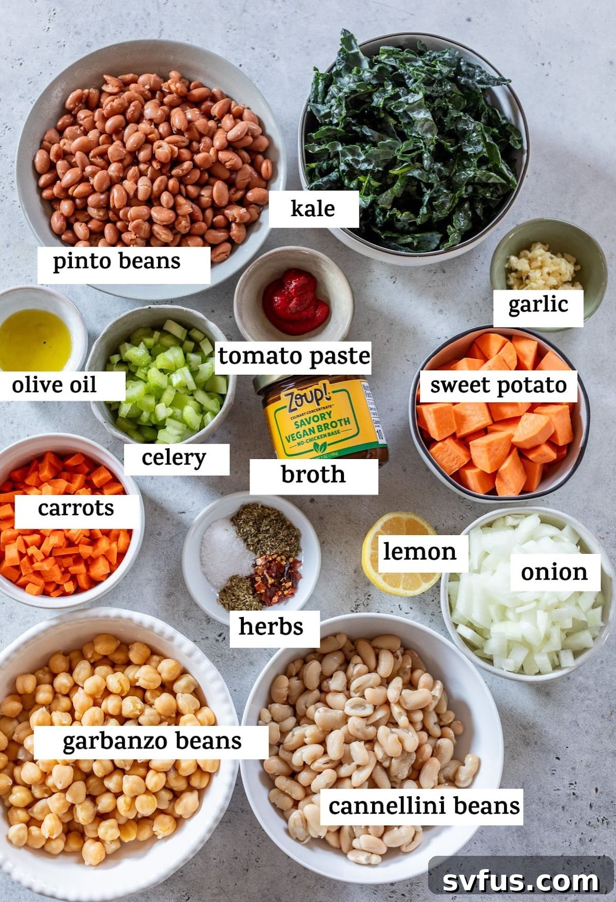 A collection of fresh ingredients laid out for making three bean soup, including various beans, sweet potato, kale, and aromatic vegetables.