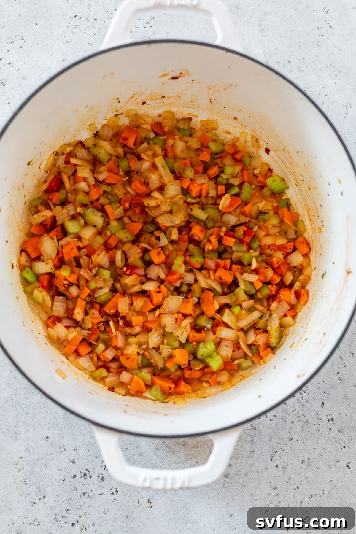 Diced onions, carrots, and celery sautéing in olive oil in a white Dutch oven, forming the aromatic base for the soup.