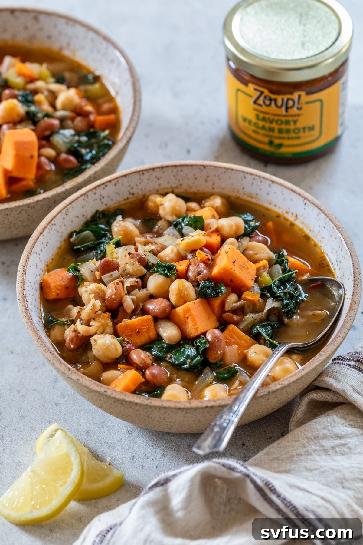 Two steaming bowls of hearty three bean soup, garnished with fresh herbs, alongside lemon slices.