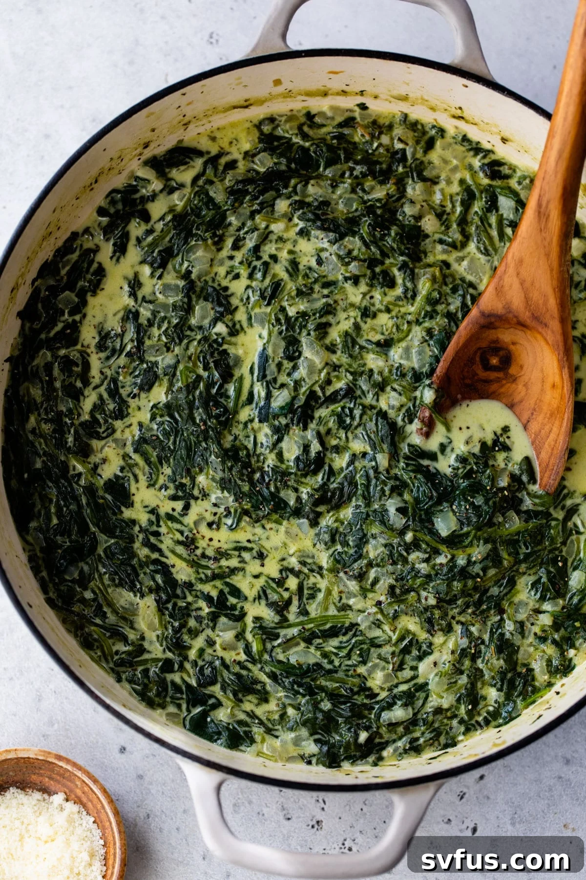 creamed spinach simmering in a dutch oven with a wooden spoon