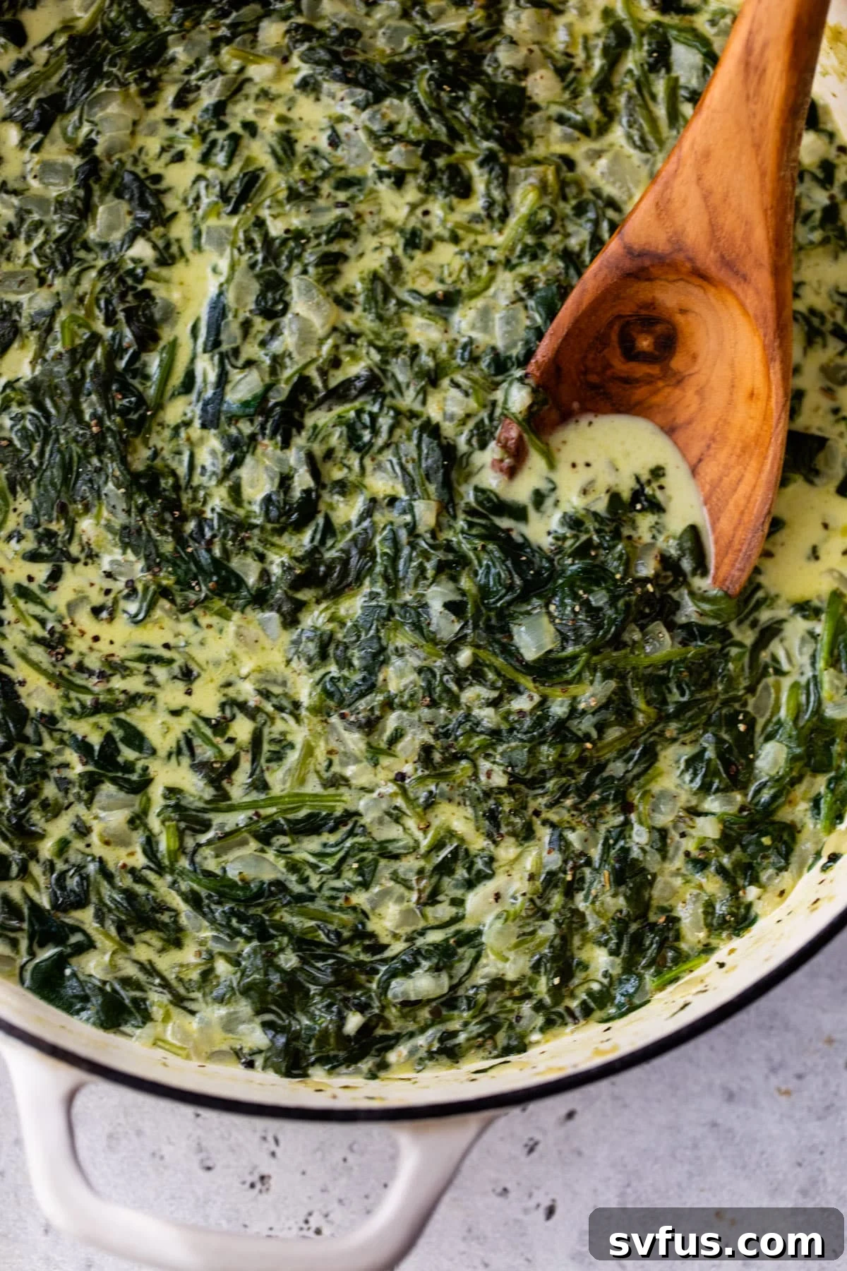 close-up of creamed spinach in a dutch oven with a wooden spoon, ready to serve