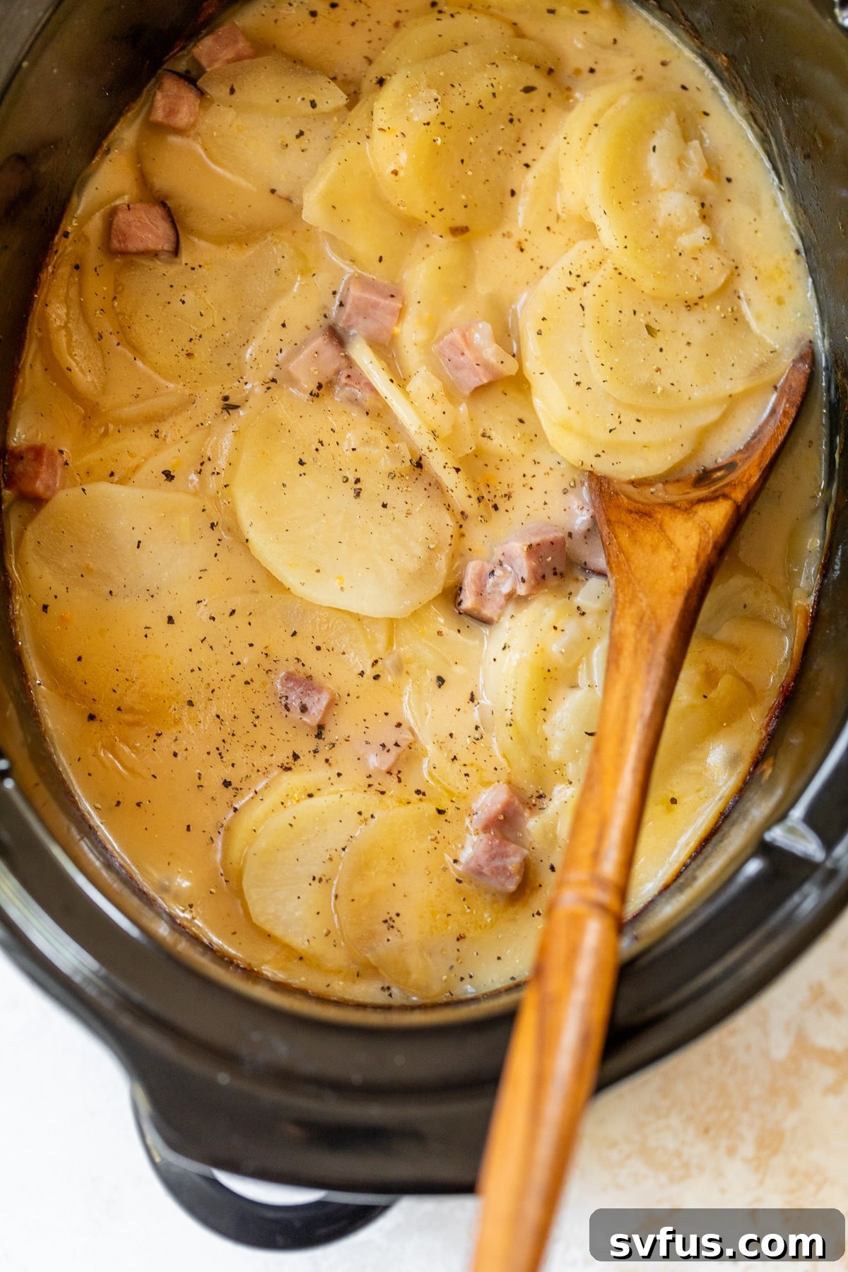 cooked scalloped potatoes and ham in a crockpot with a wooden spoon, ready to be served
