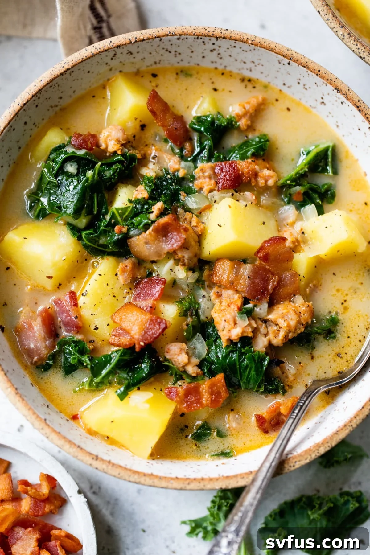 A steaming bowl of Whole30 Zuppa Toscana soup with a spoon, garnished with fresh kale and crispy bacon.