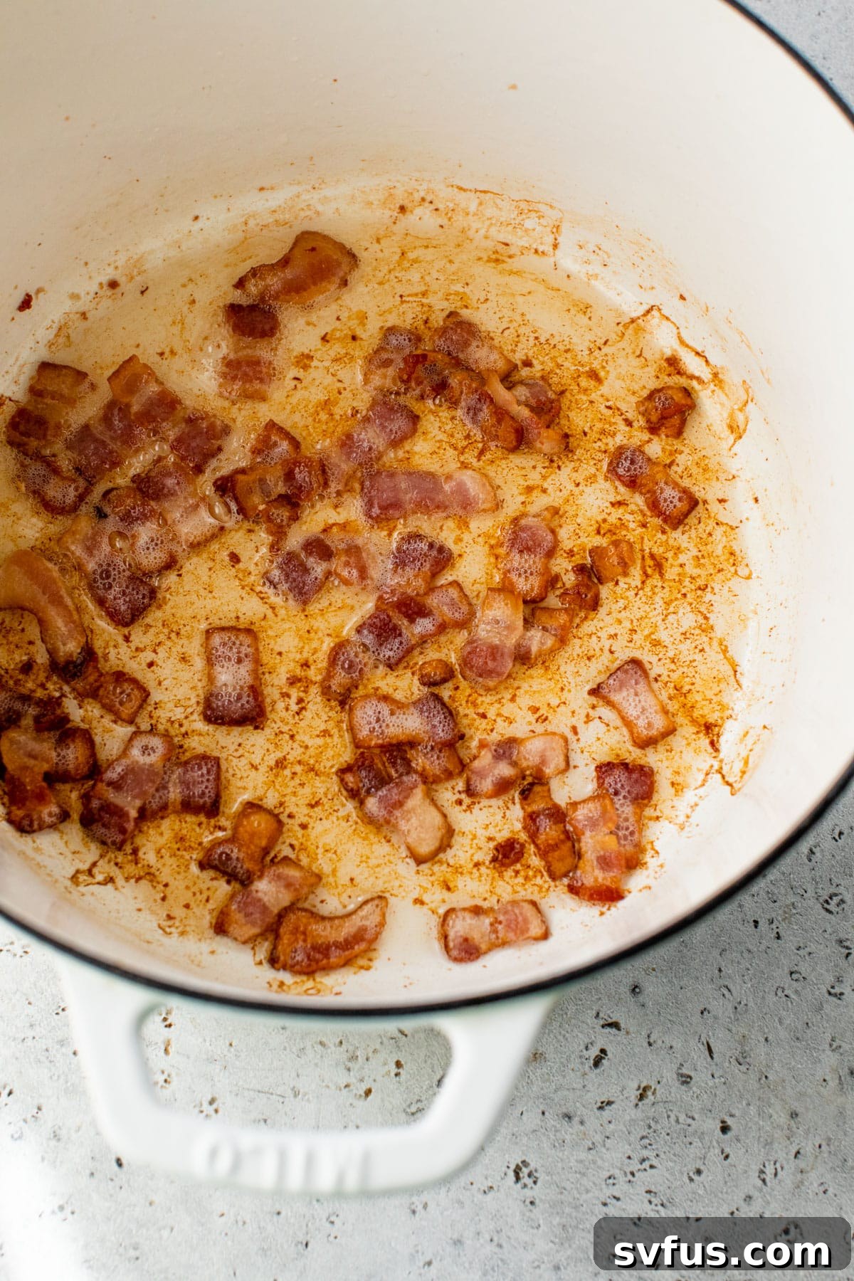 Crispy bacon cooking in a Dutch oven, rendering fat beautifully.