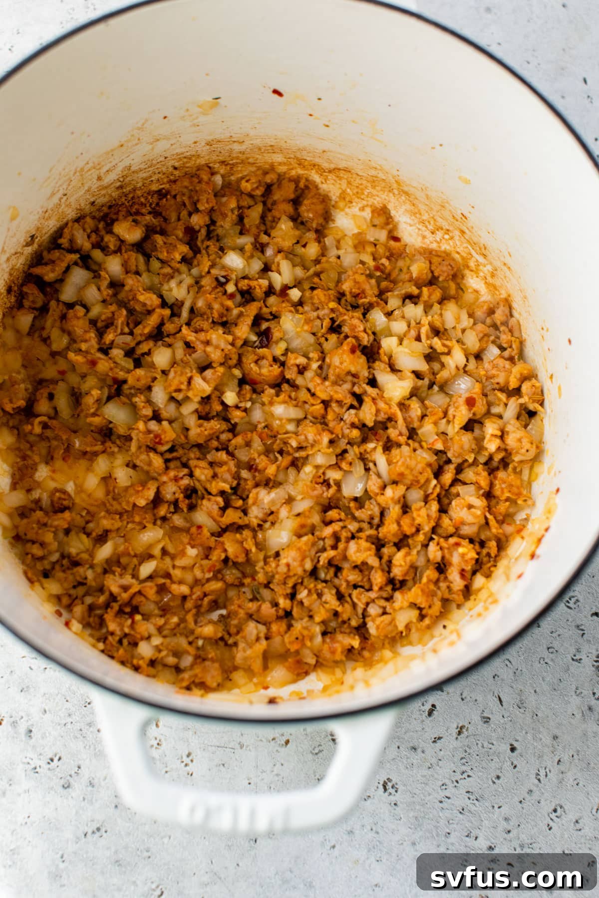 Spicy chicken sausage and diced onion sautéing in a Dutch oven, creating a fragrant base.