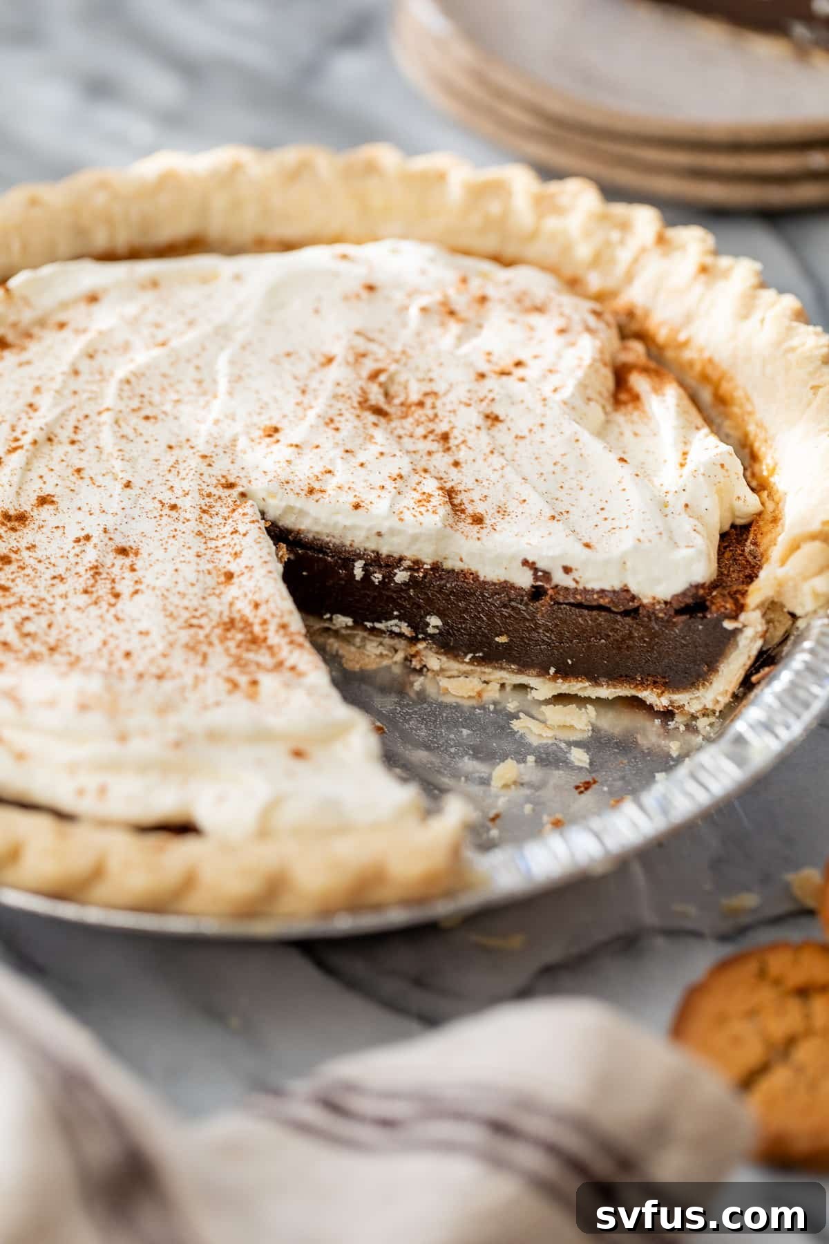 A close-up side view of a gingerbread pie with a slice carefully removed, showing its creamy filling and whipped cream topping.