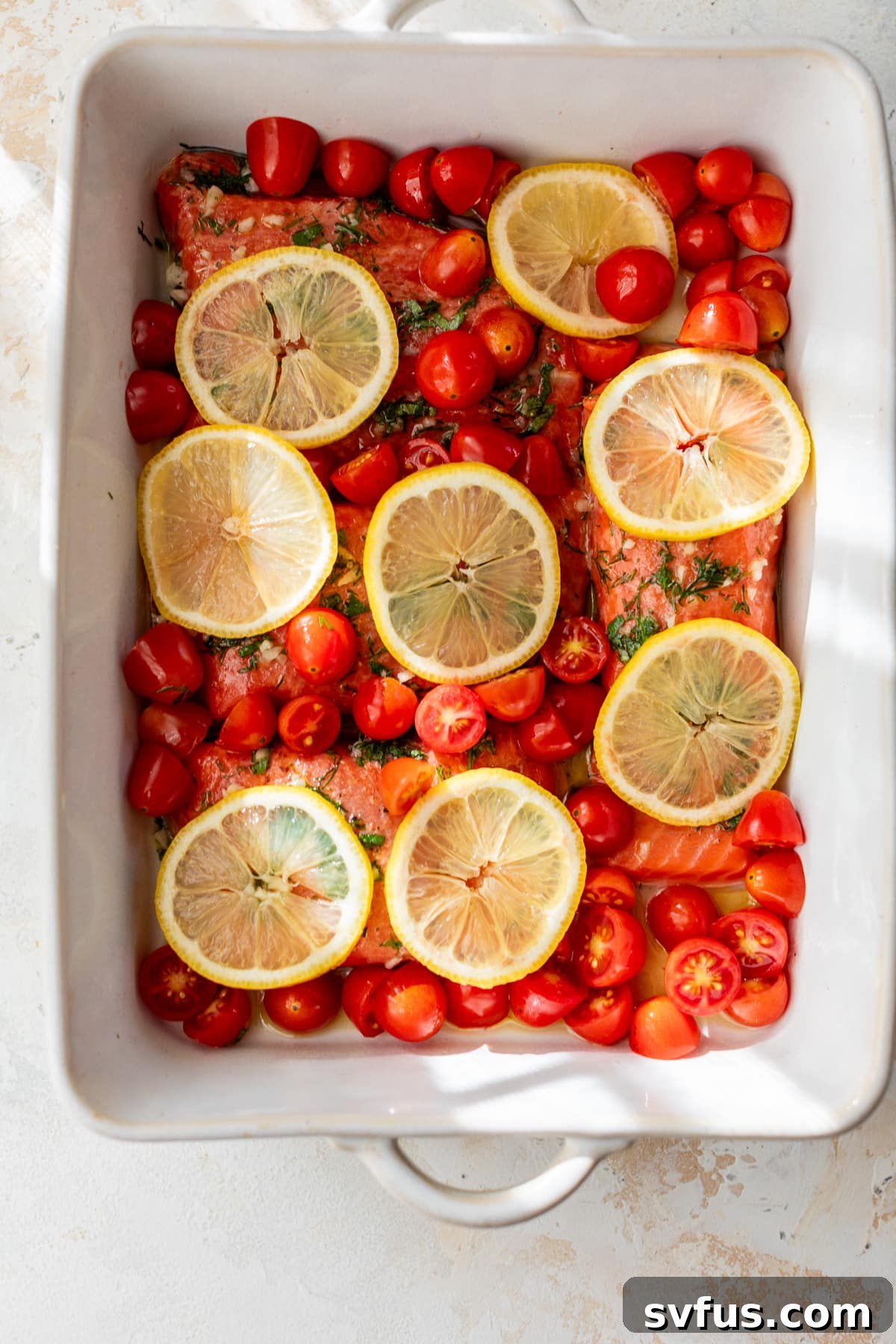 greek salmon in a baking dish topped with lemon slices and grape tomatoes