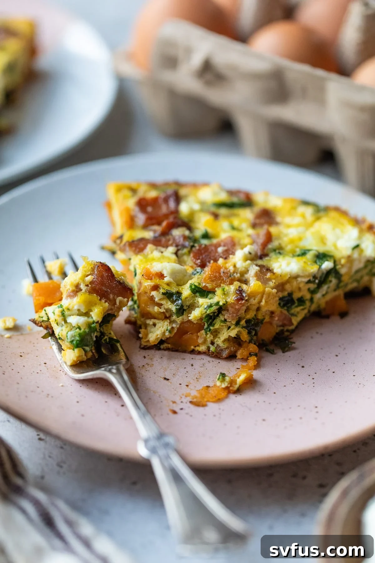 A perfectly cooked slice of sweet potato frittata on a white plate with a bite taken out, showing the layers of ingredients.
