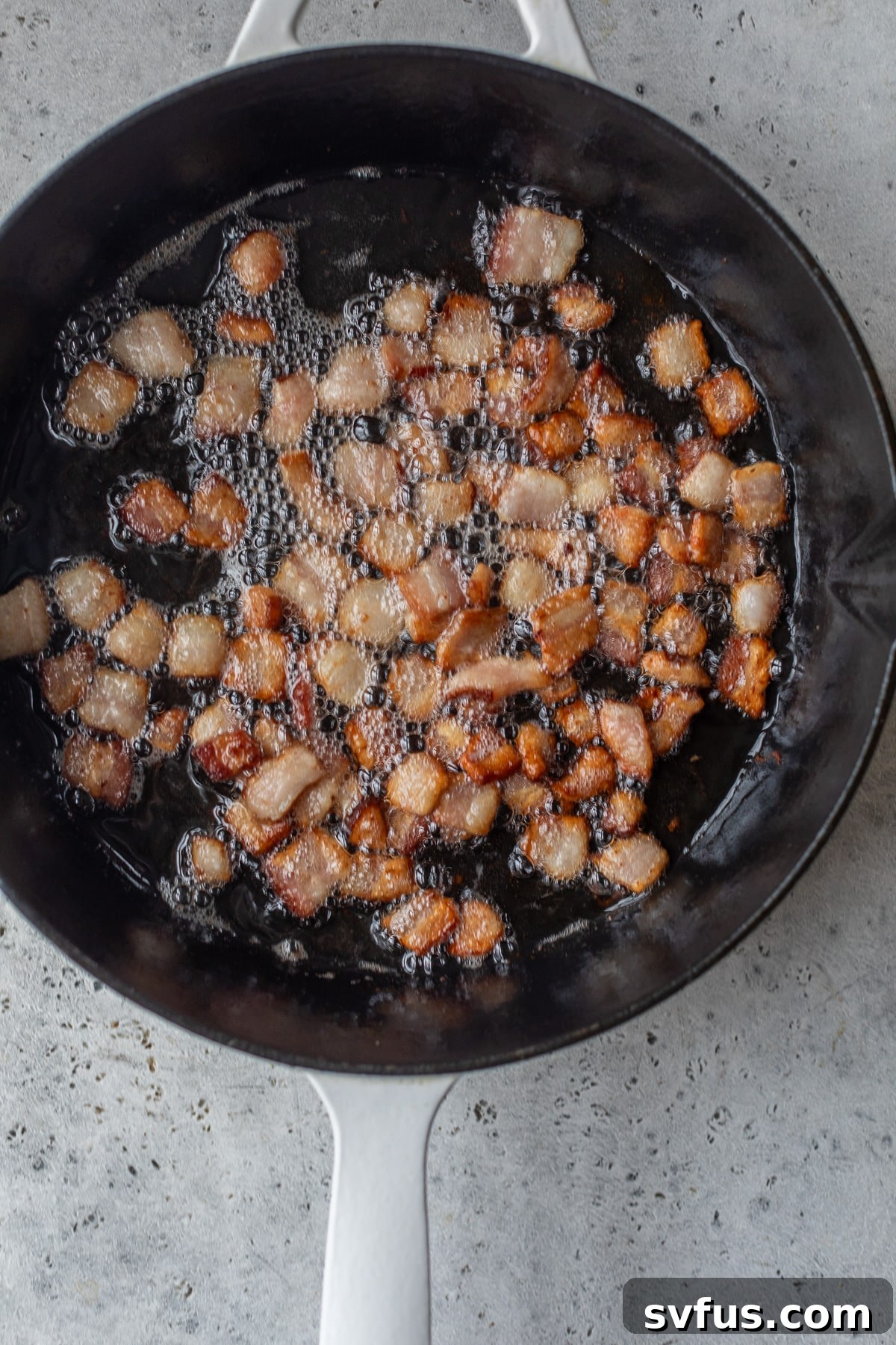Chopped bacon pieces sizzling and cooking in a cast iron skillet, turning golden brown and crispy.