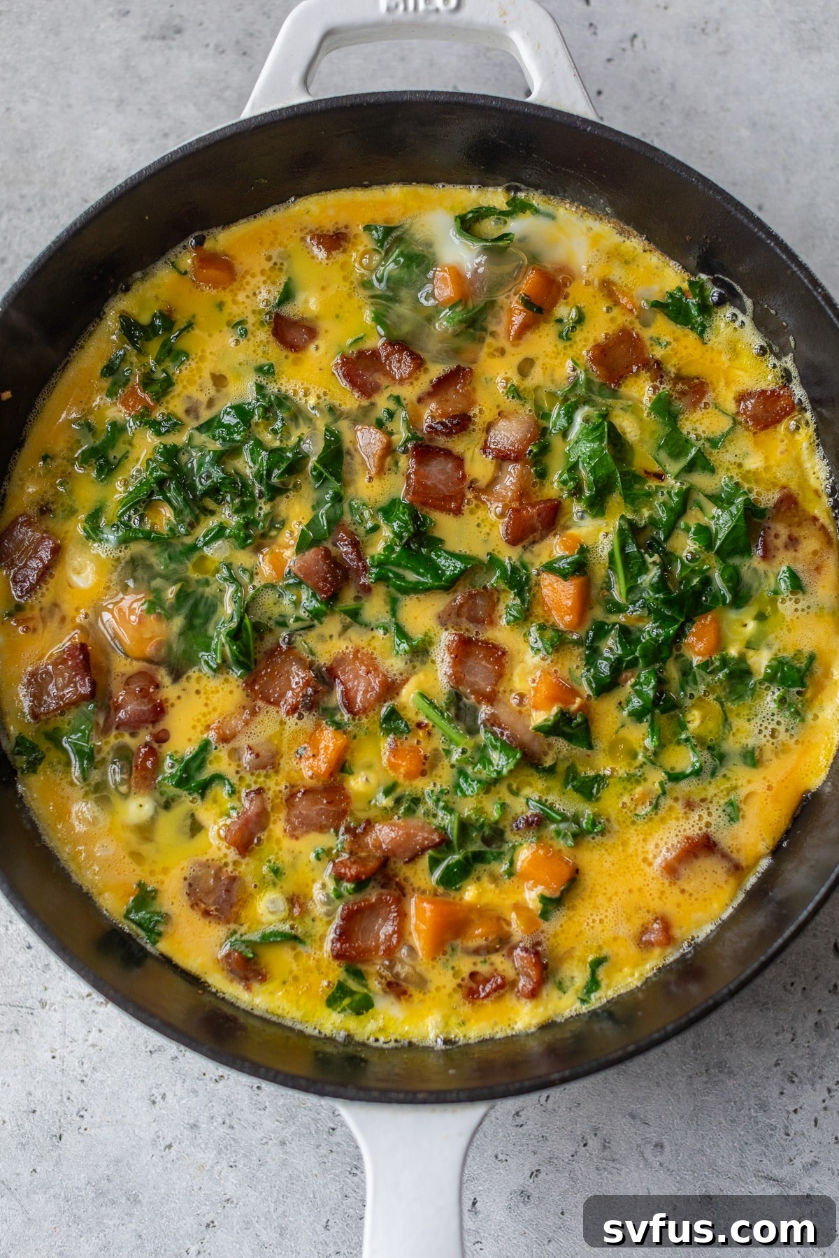 An uncooked sweet potato frittata mixture, with eggs, vegetables, and bacon, prepared in a cast iron skillet before baking.