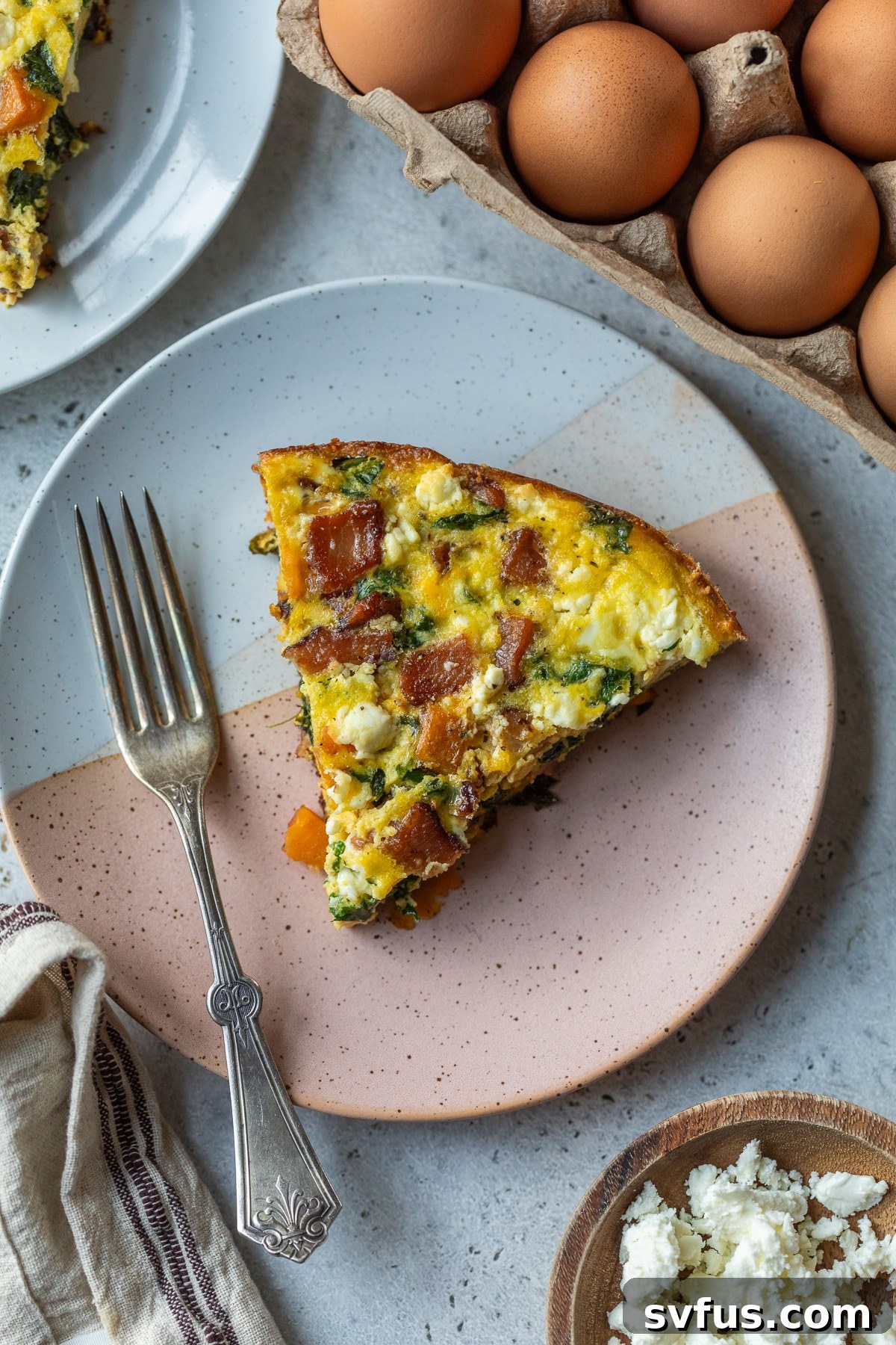 A golden-brown slice of sweet potato frittata on a white plate, ready to be eaten with a fork.