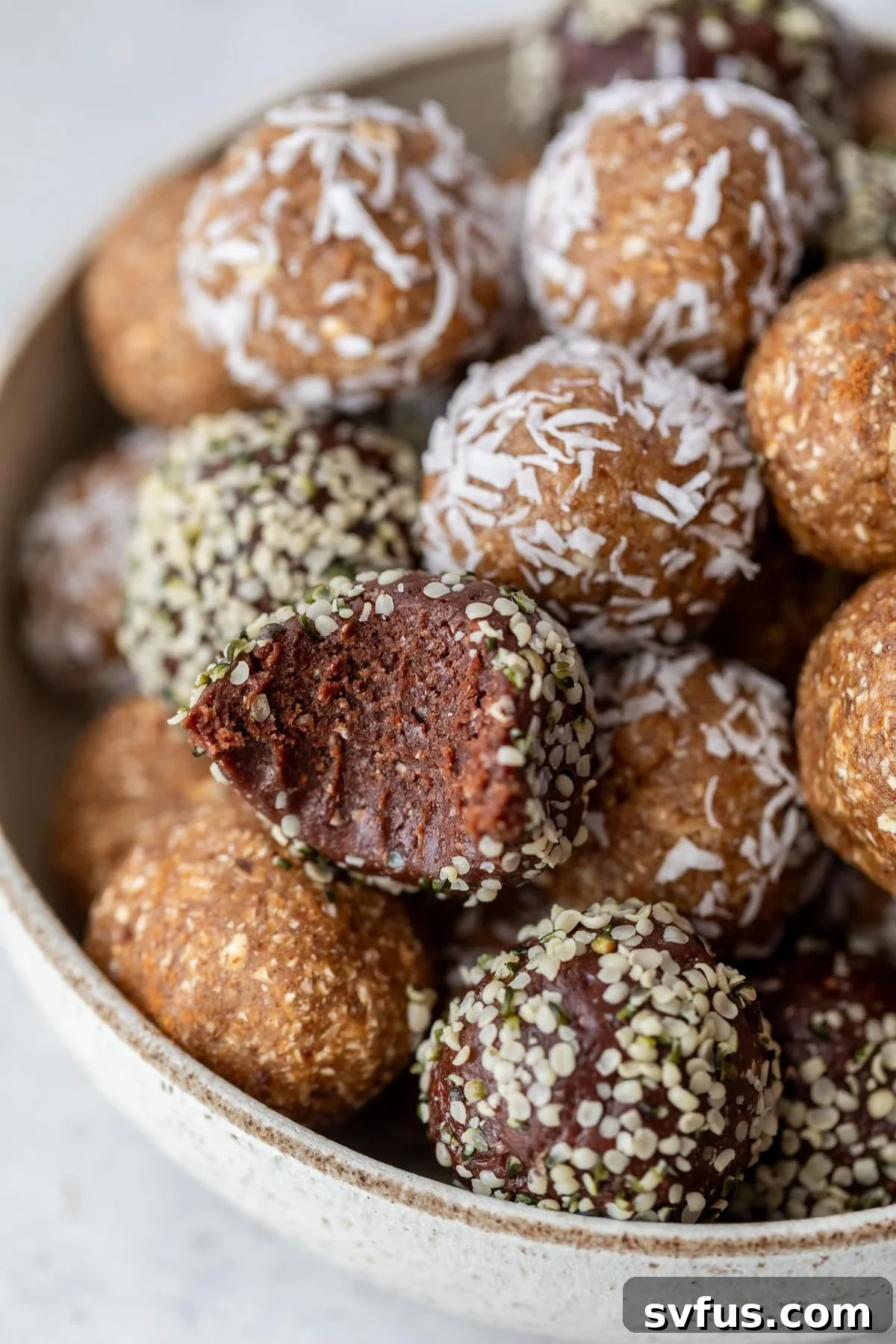 A bowl filled with various date energy balls, with one ball bitten into, revealing its chewy texture. A perfect healthy snack.