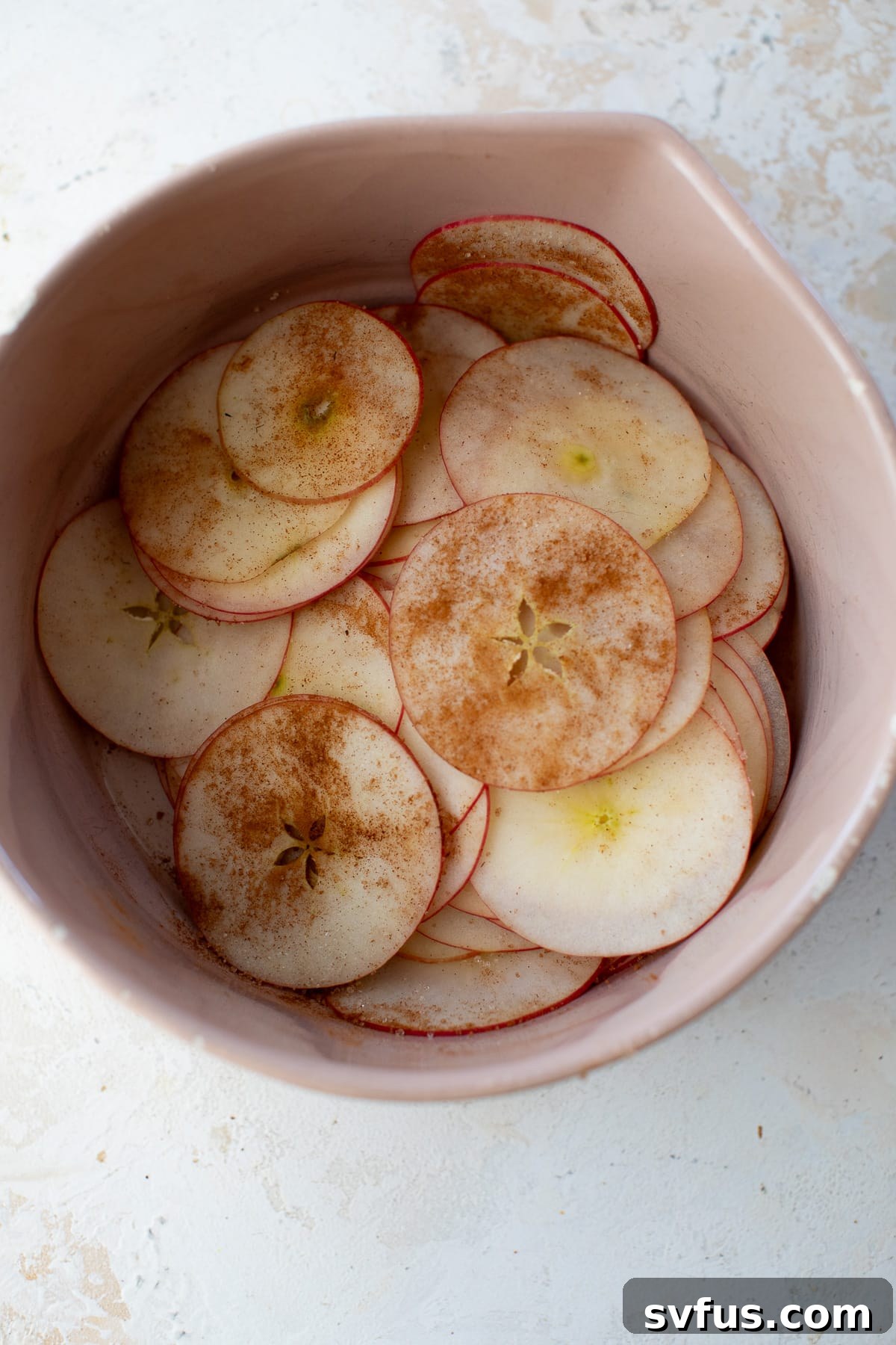 Apple slices in a mixing bowl, generously sprinkled with cinnamon sugar, ready to be tossed.
