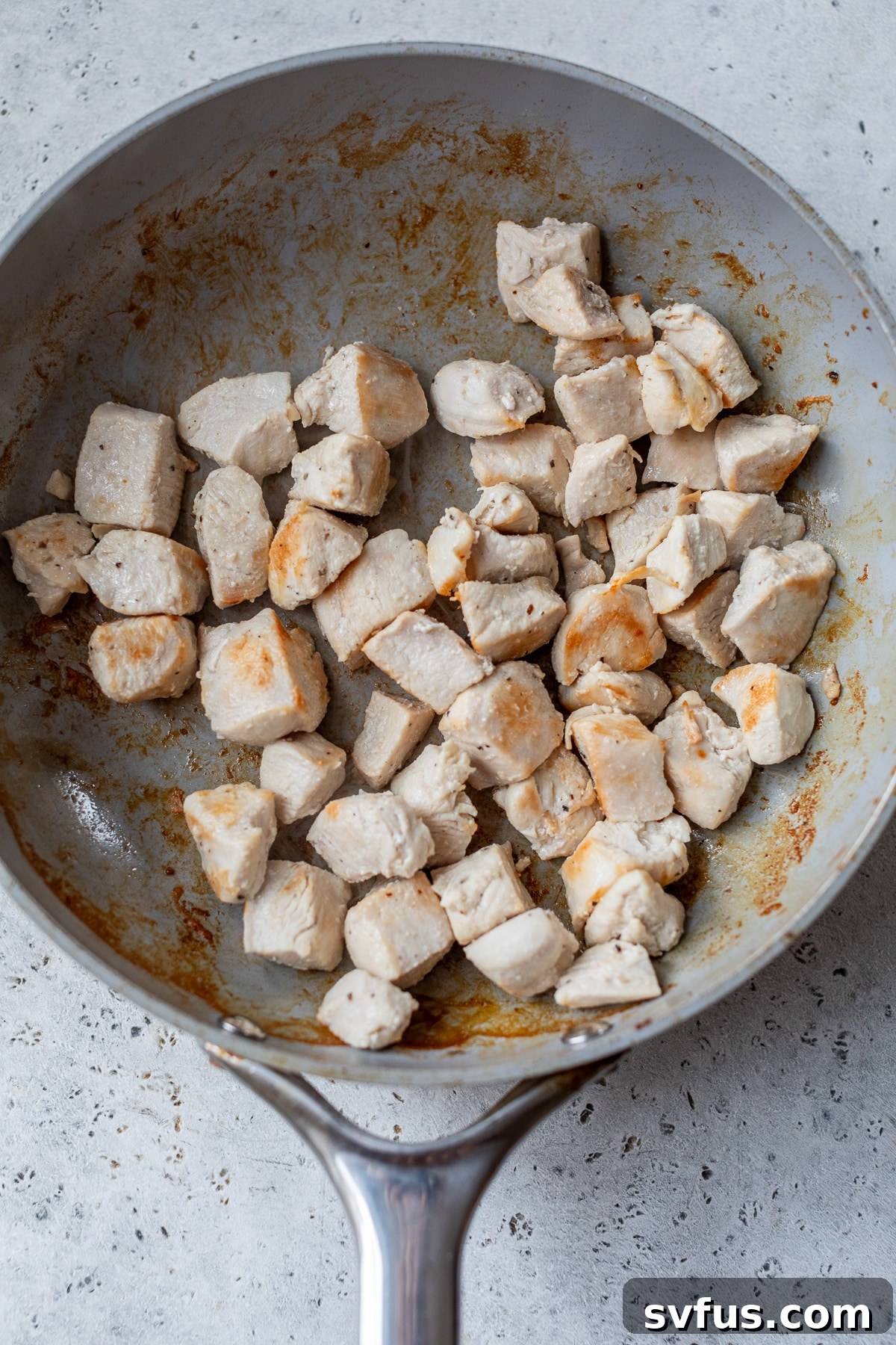 Diced chicken pieces cooking in a skillet until golden brown