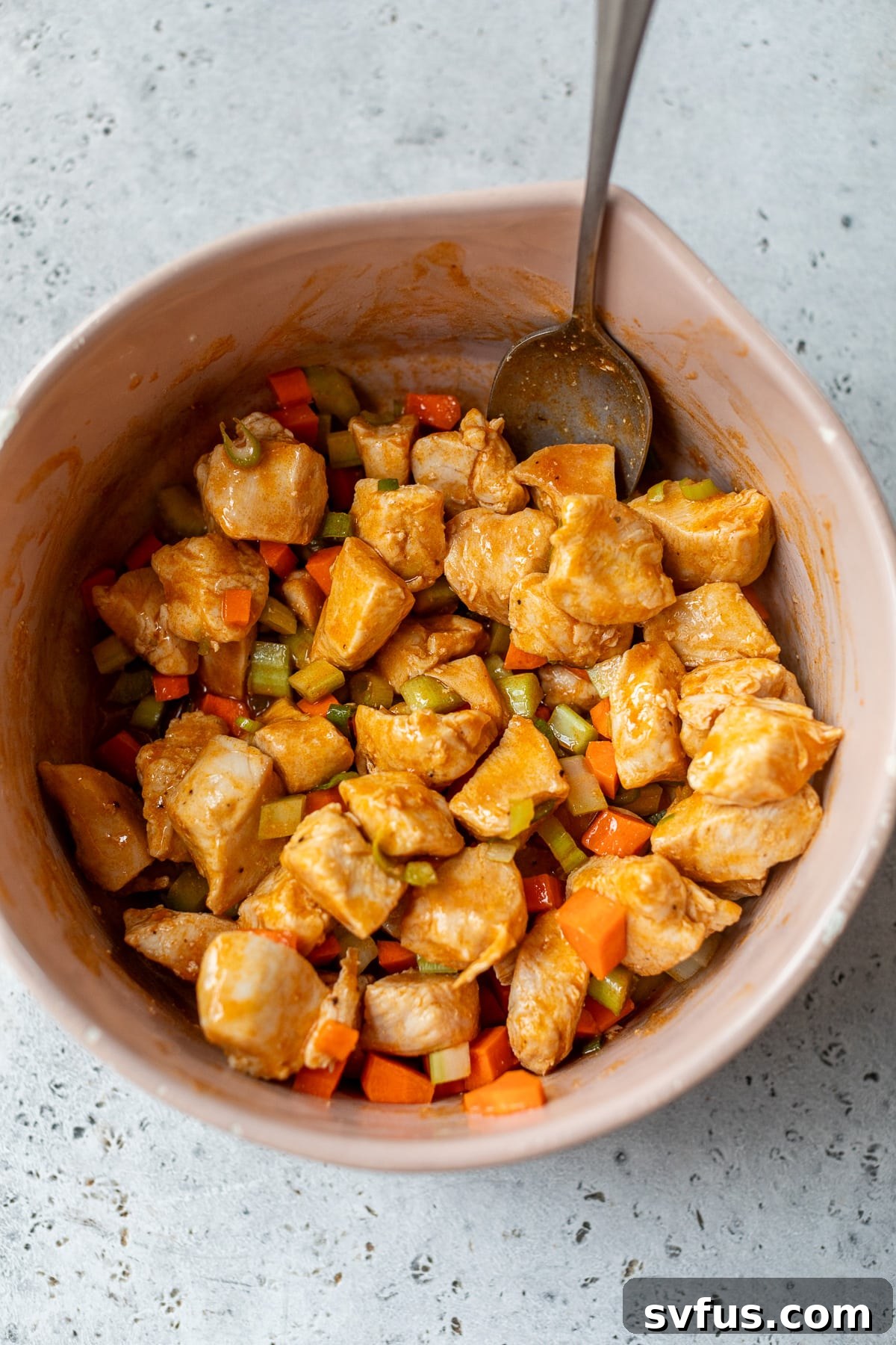 Cooked chicken pieces and chopped vegetables mixed with buffalo sauce in a bowl