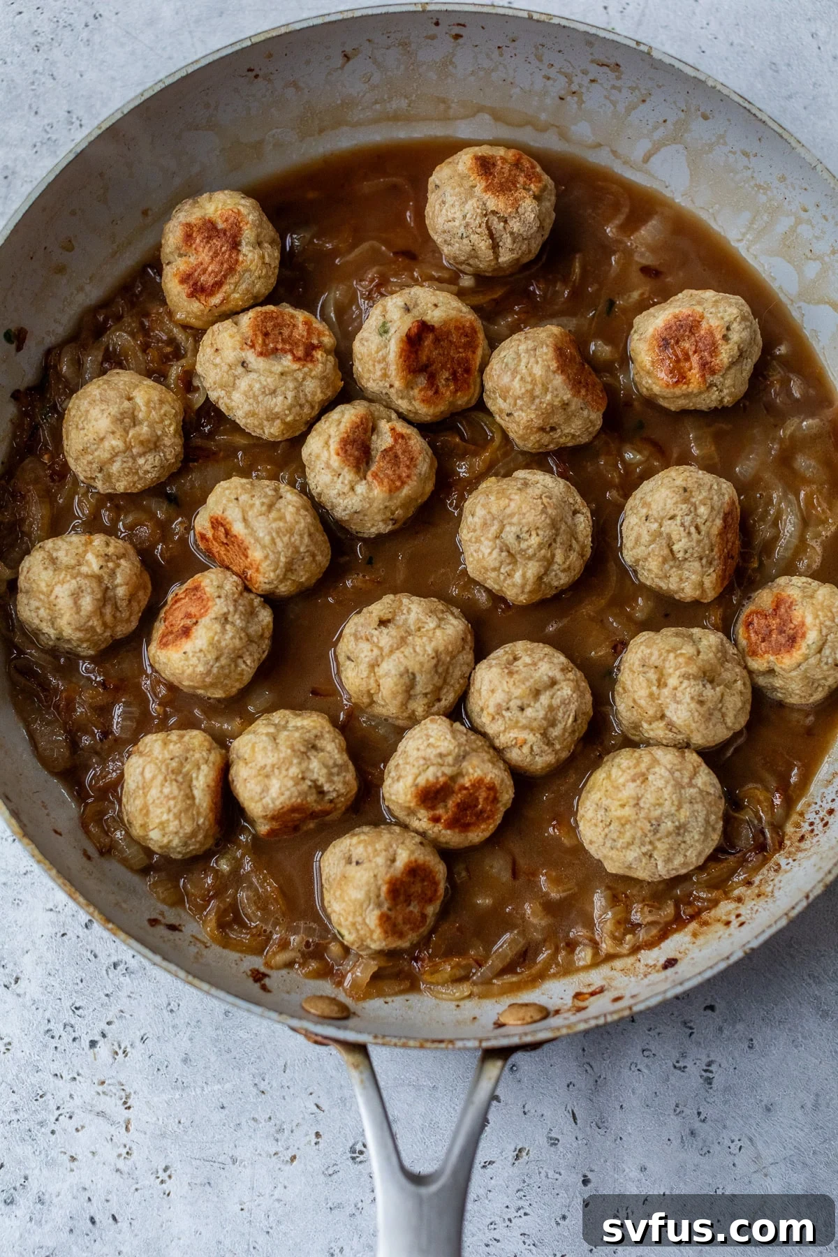 meatballs placed in a skillet with caramelized onions and french onion sauce poured over top