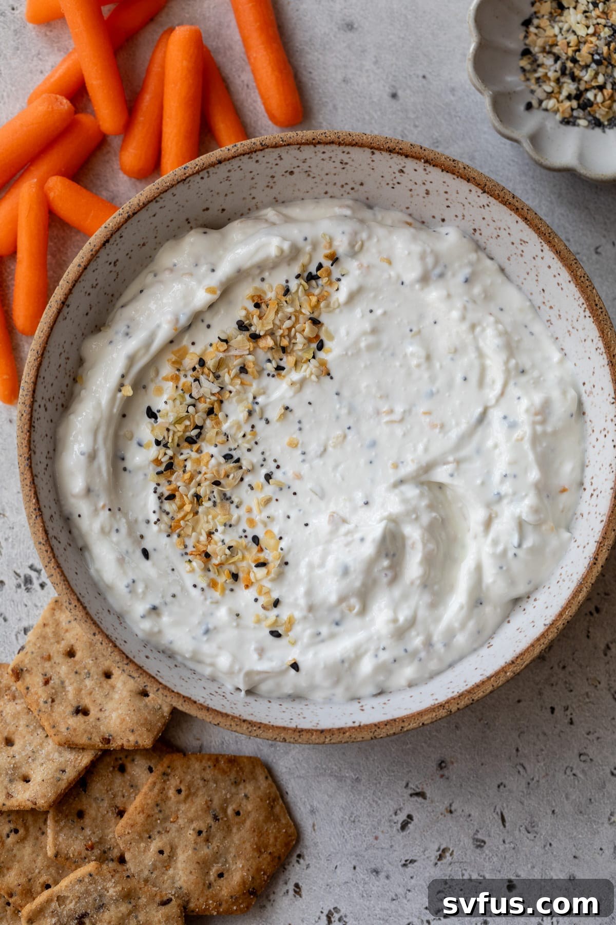 A bowl of everything bagel dip with fresh carrot sticks arranged neatly on the side, highlighting the dip's appealing texture.