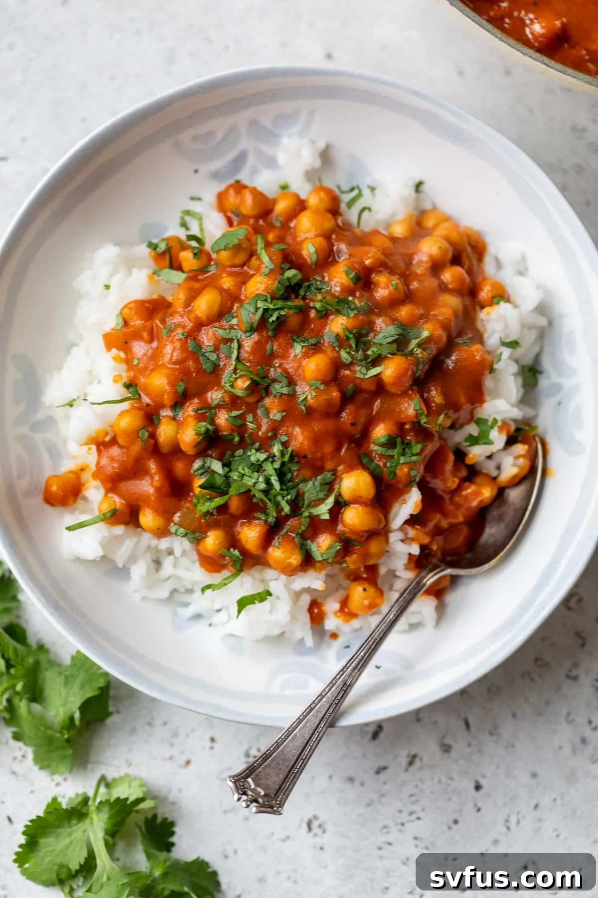 A bowl of creamy vegan butter chickpeas served over fluffy basmati rice, garnished with fresh cilantro and a spoon resting in the bowl.