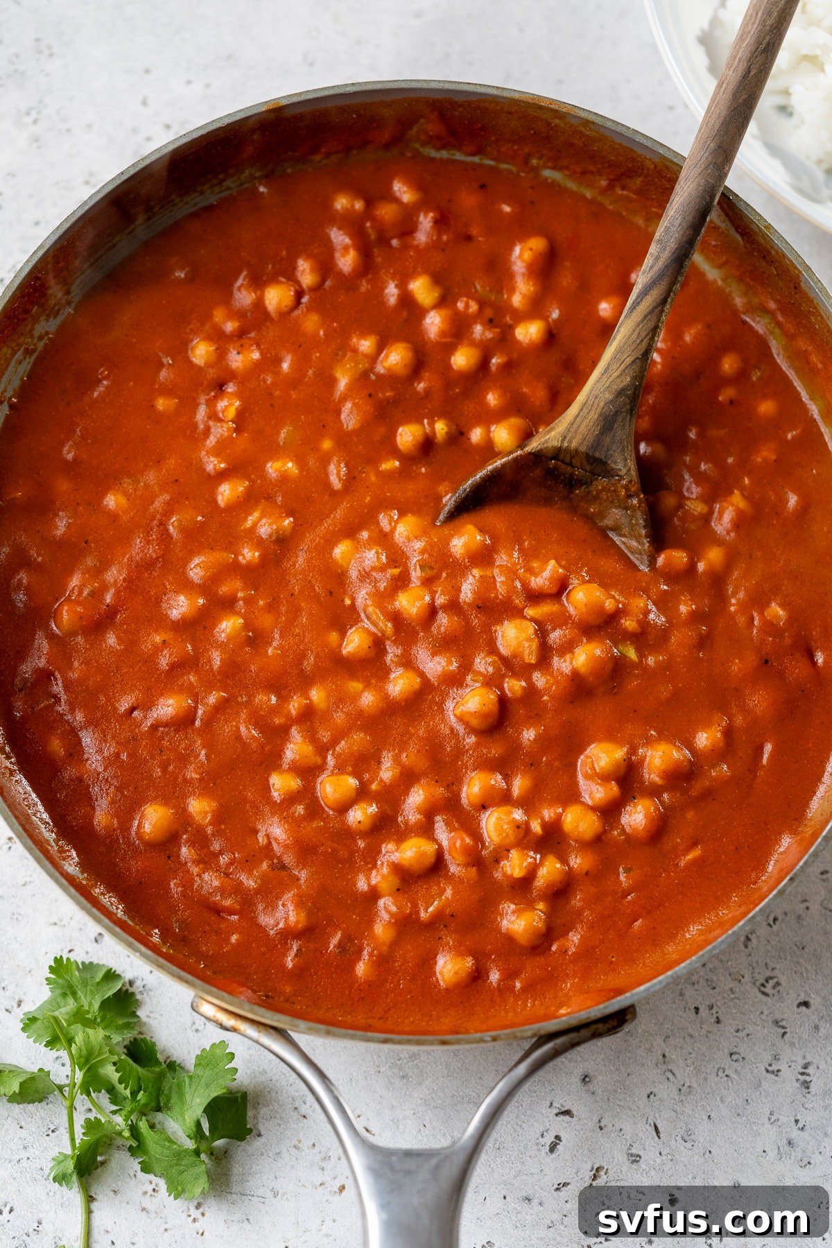 A rustic cast-iron skillet filled with vibrant, creamy vegan butter chickpeas, ready to be served, with a wooden spoon resting in the rich curry.