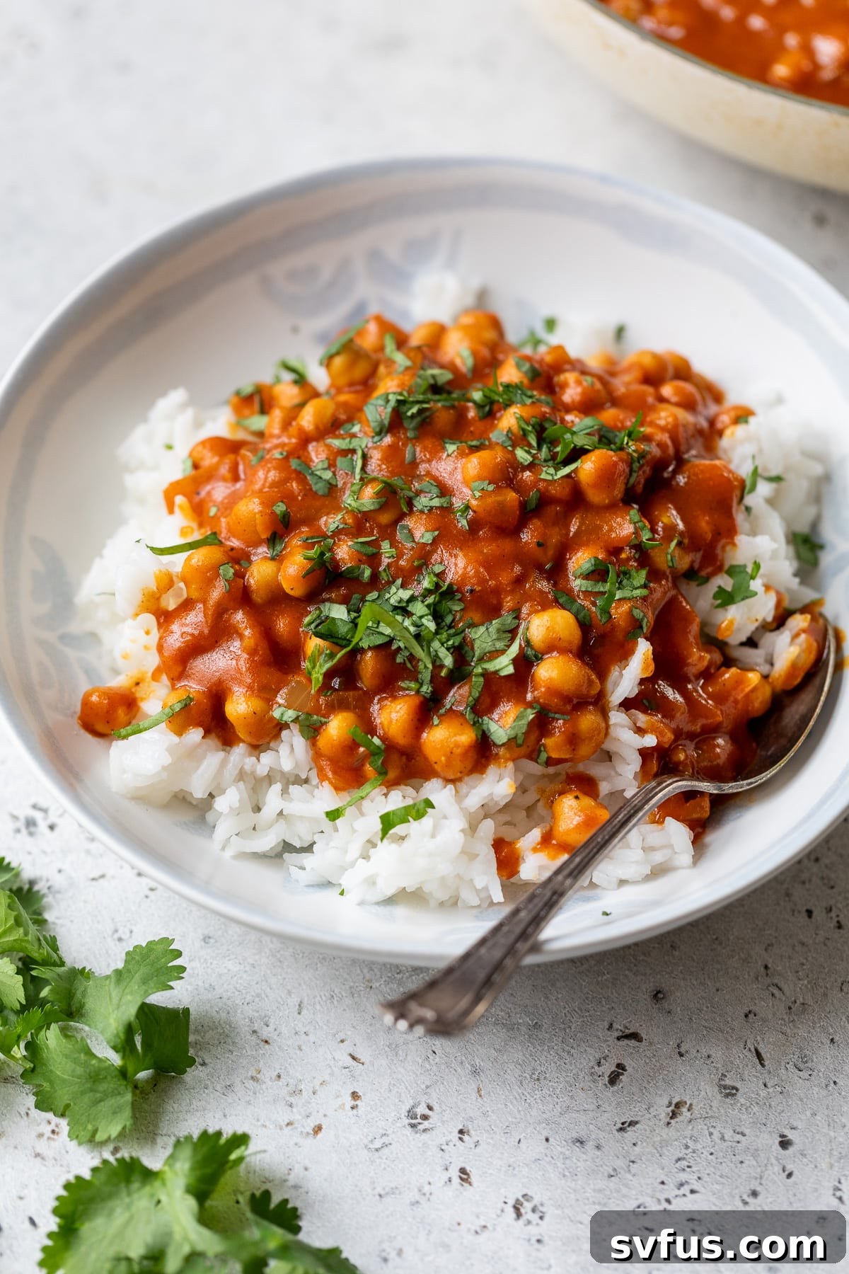 Another enticing image of creamy vegan butter chickpeas served over white rice in a bowl, garnished with fresh cilantro, ready to be enjoyed with a spoon.