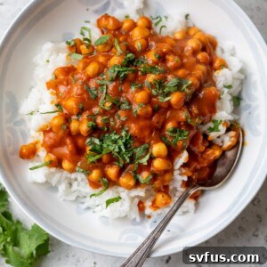 A vibrant bowl of vegan butter chickpeas served over fluffy white rice, garnished with fresh green cilantro leaves.