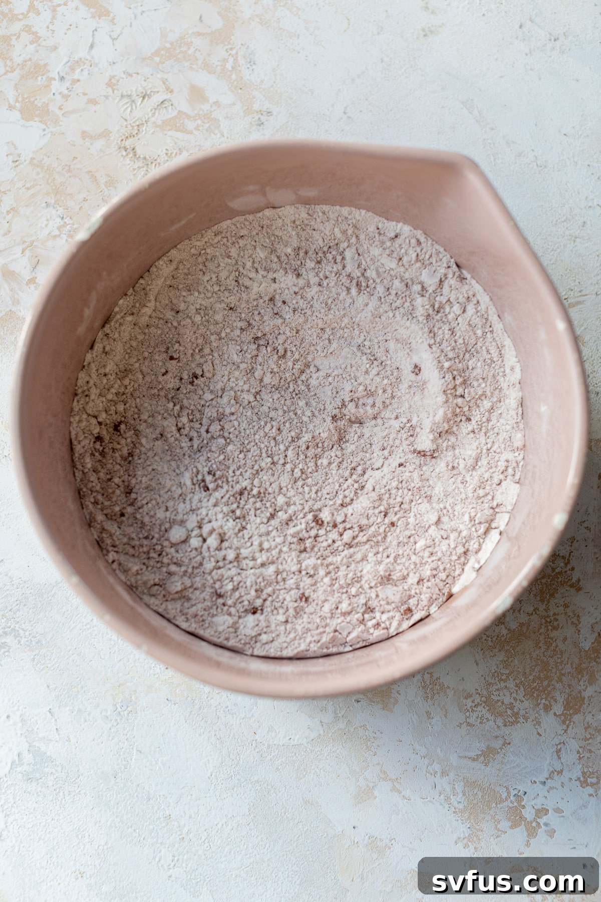 A large bowl containing dry ingredients like flour, cocoa powder, baking powder, baking soda, and salt, ready to be mixed for red velvet cupcakes.