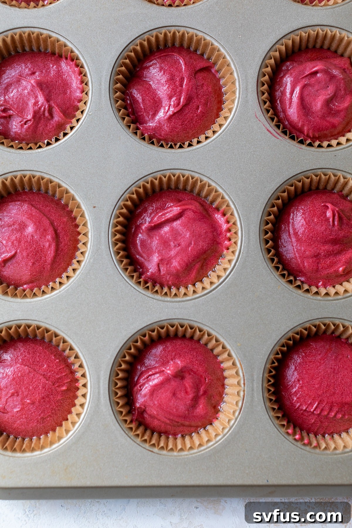 Red velvet cupcake batter neatly poured into liners within a muffin tin, ready for baking.