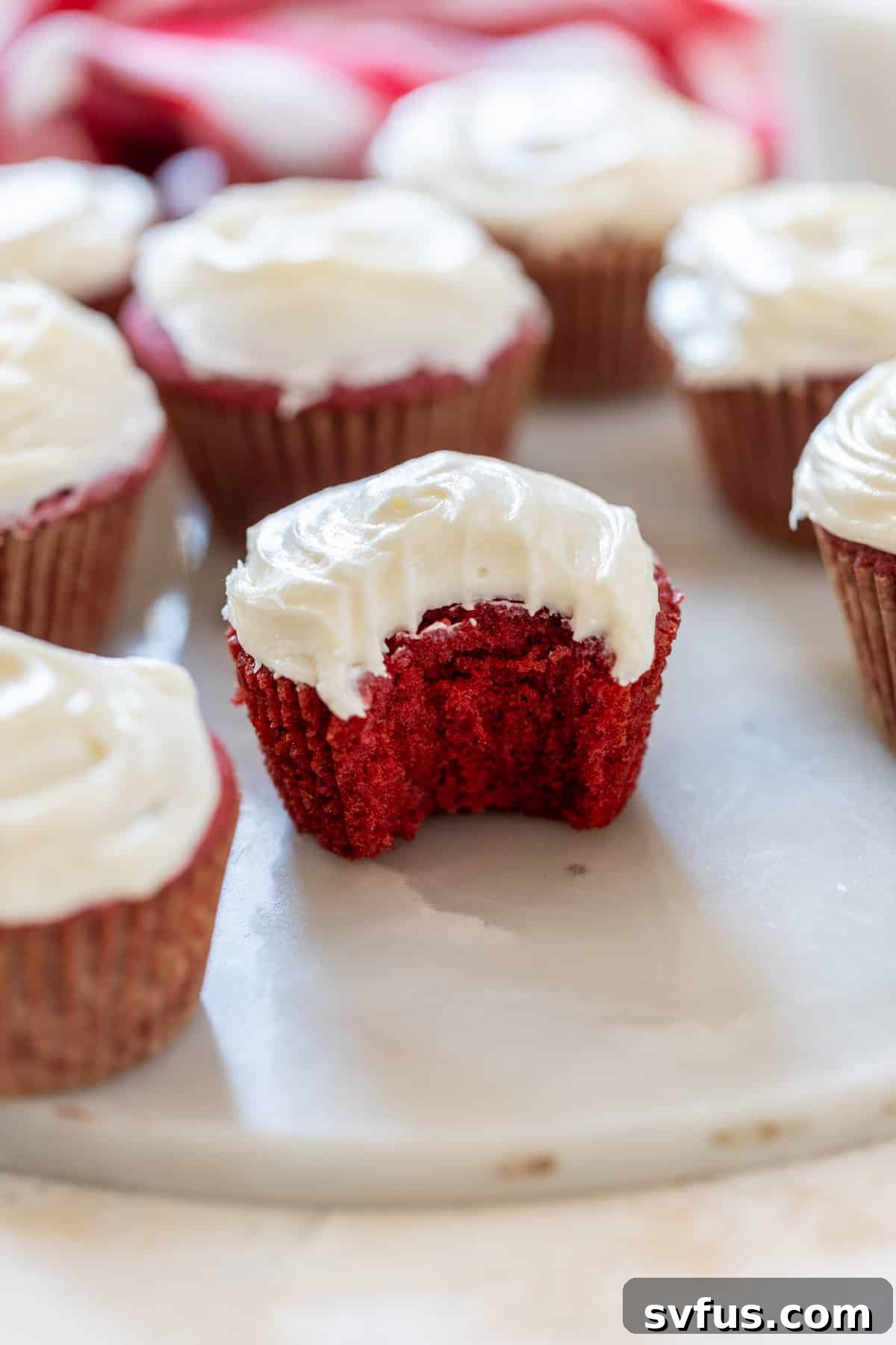 A close-up shot of a red velvet cupcake with a bite taken out, showcasing the moist cake and rich cream cheese frosting.
