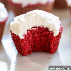 A red velvet cupcake with a bite taken out, showcasing the moist texture and creamy frosting.